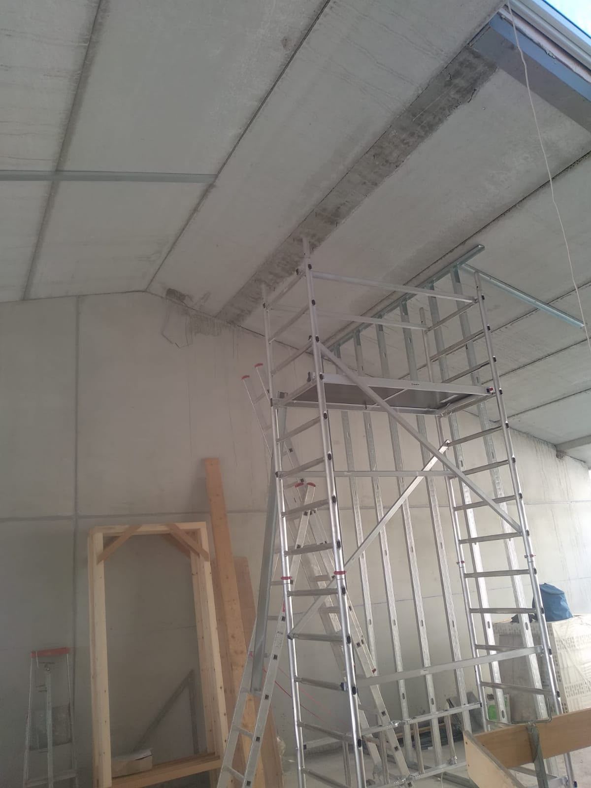 Habitación interior con andamios metálicos y una escalera bajo un techo parcialmente sin terminar.