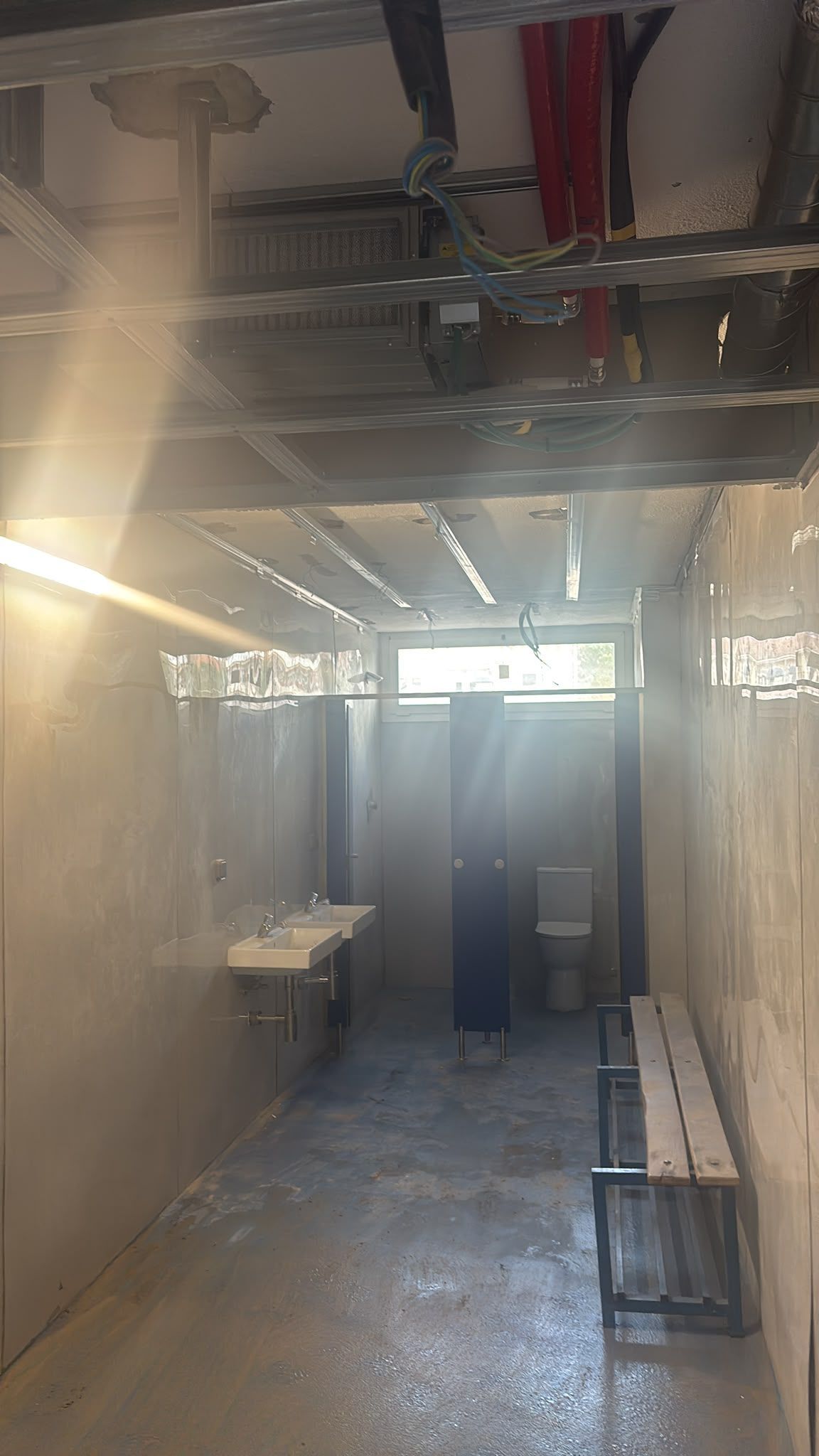 Pasillo estrecho y sin terminar, con tuberías del techo a la vista, escombros de construcción 
