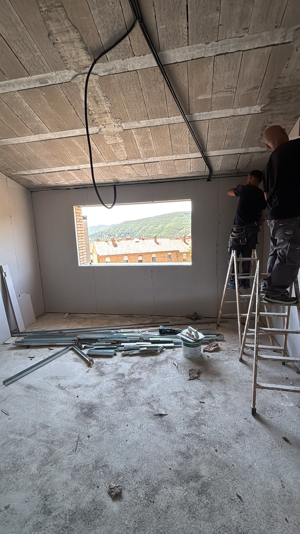 Dos trabajadores instalando un techo en una habitación sin terminar con una abertura para una ventana