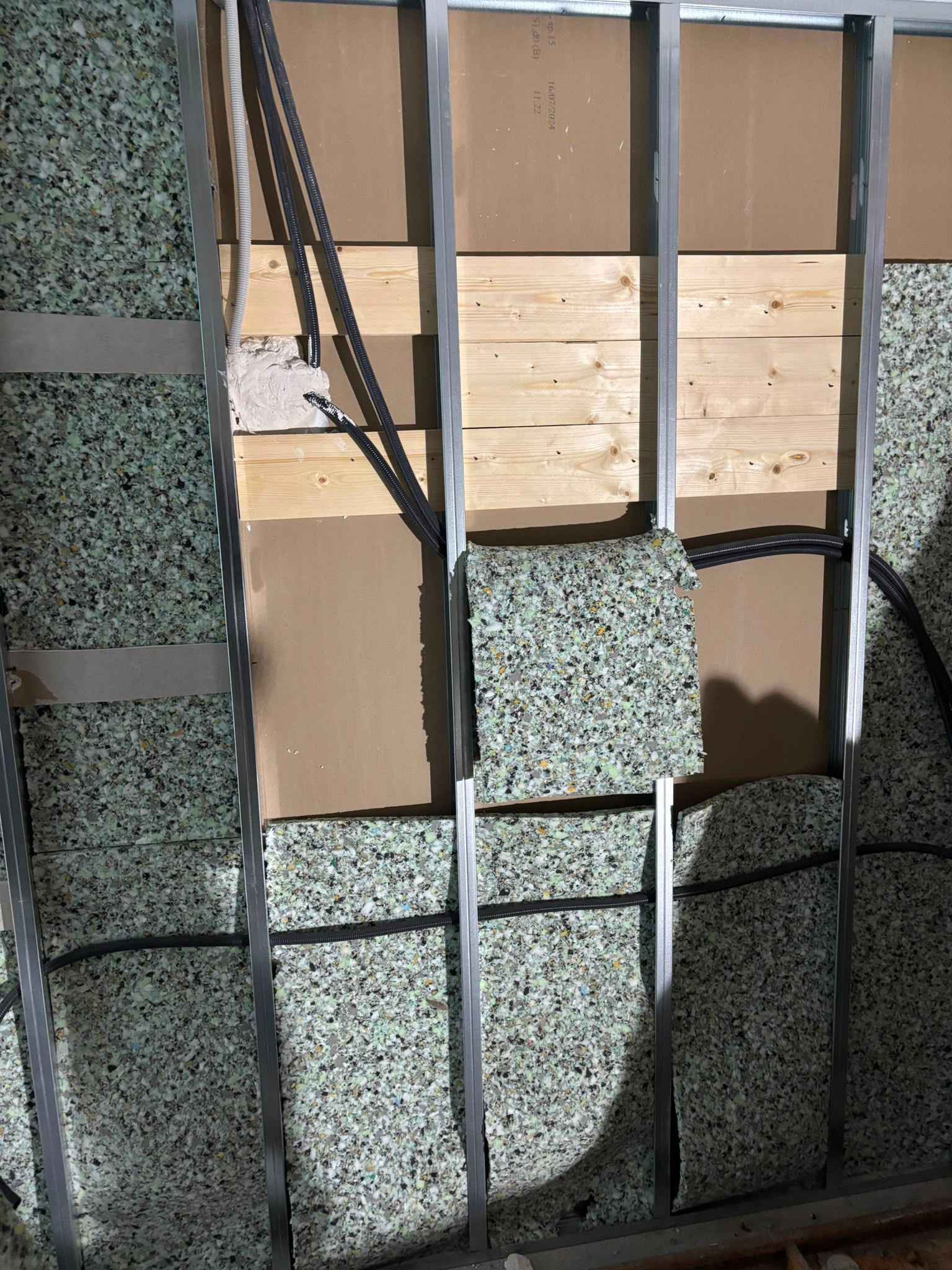 Tablero dañado que cubre una ventana rota con un panel moteado de verde y un respaldo marrón expuesto.