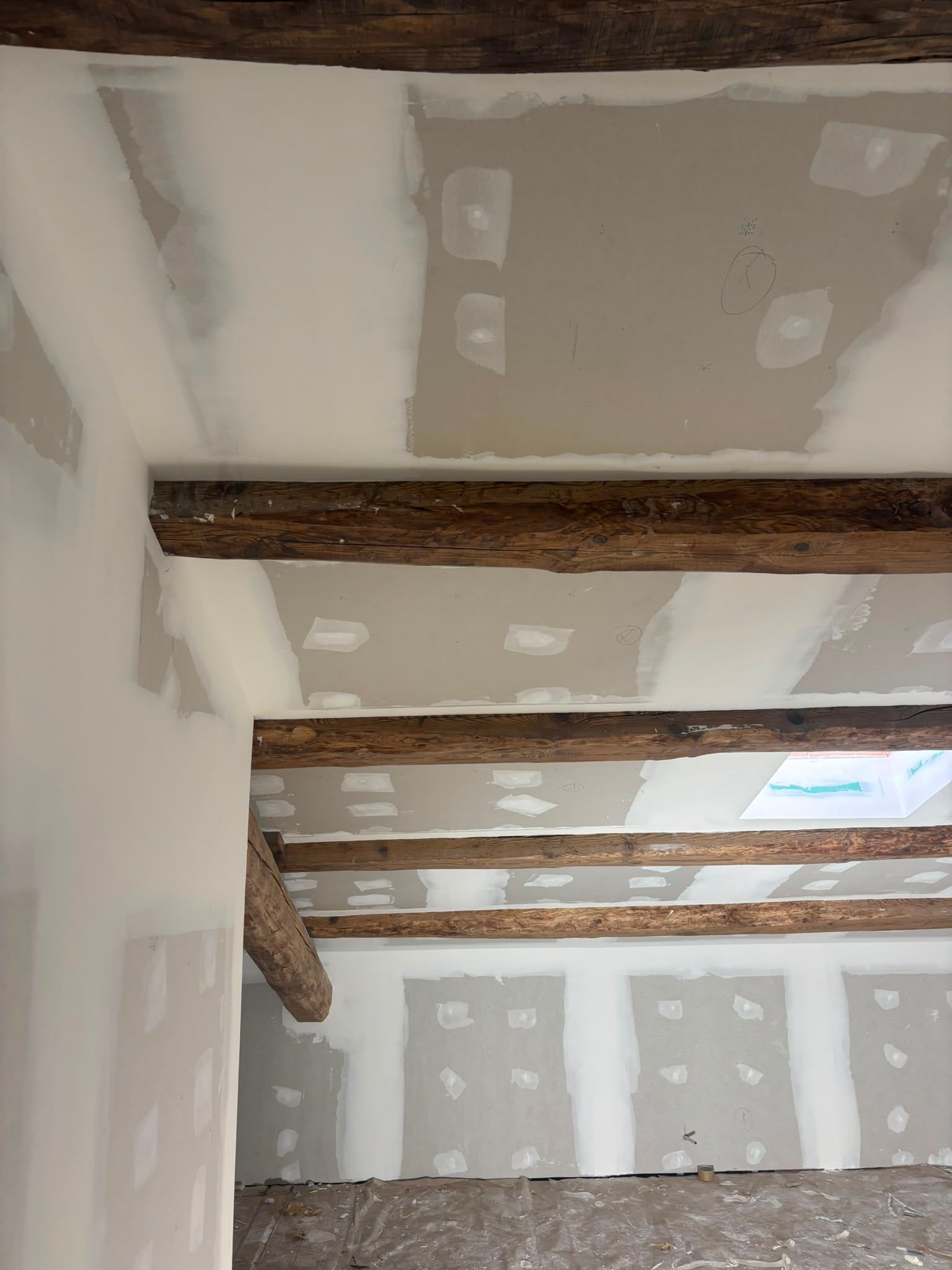 Habitación sin terminar con parches en las paredes de pladur y vigas de madera a la vista en el techo.