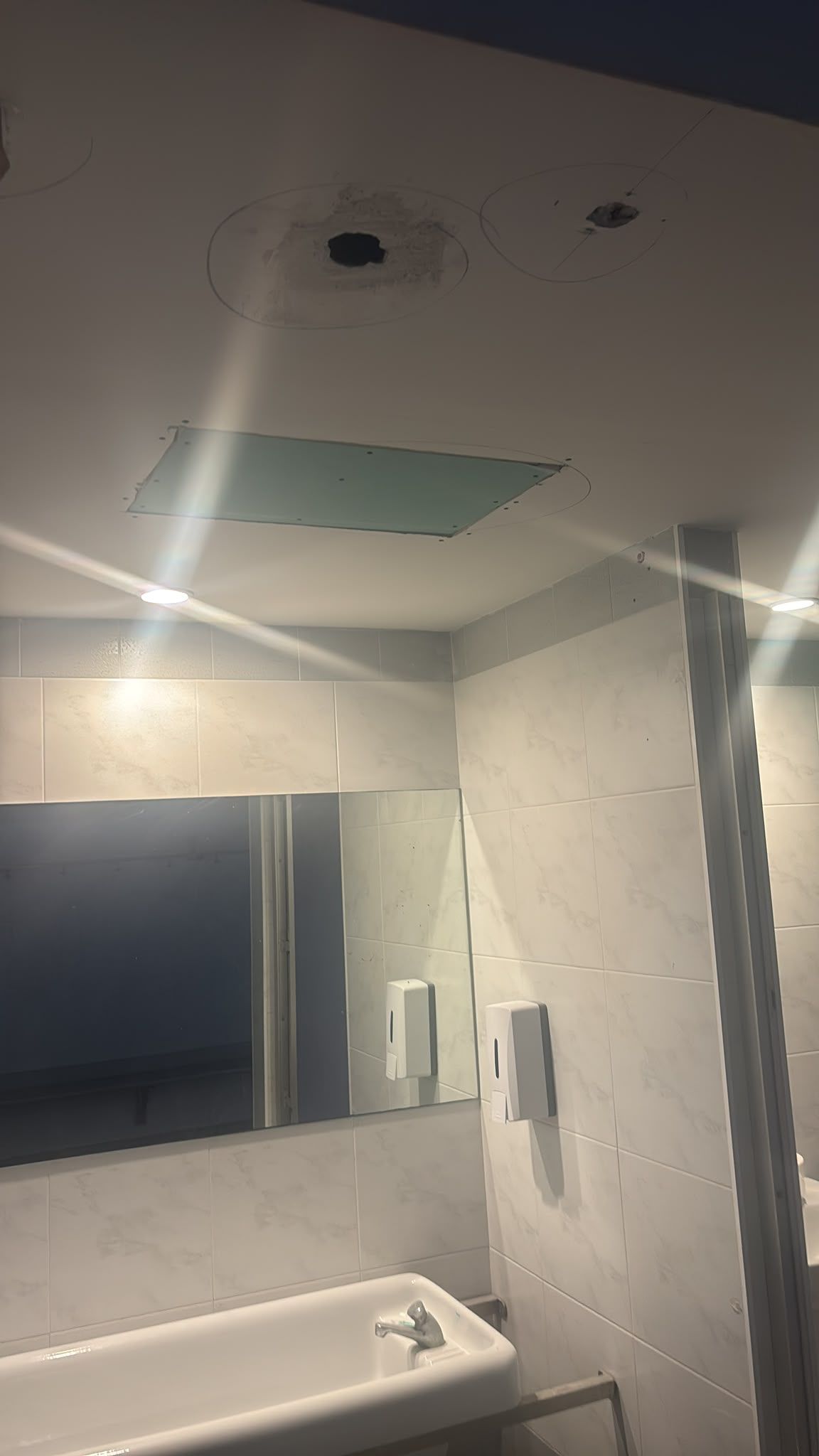 Baño con espejo, lavabo, paredes alicatadas y luces de techo reflejadas en el espejo.