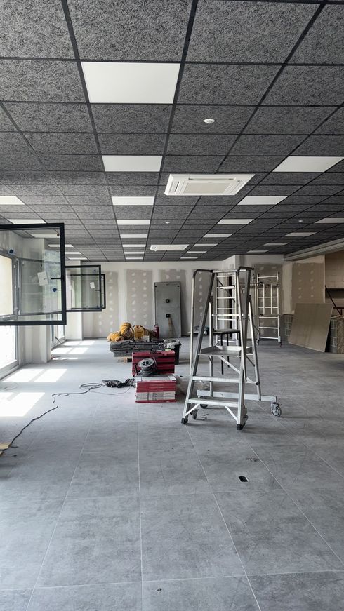 Oficina vacía en obras con escaleras, herramientas y escombros en el suelo.