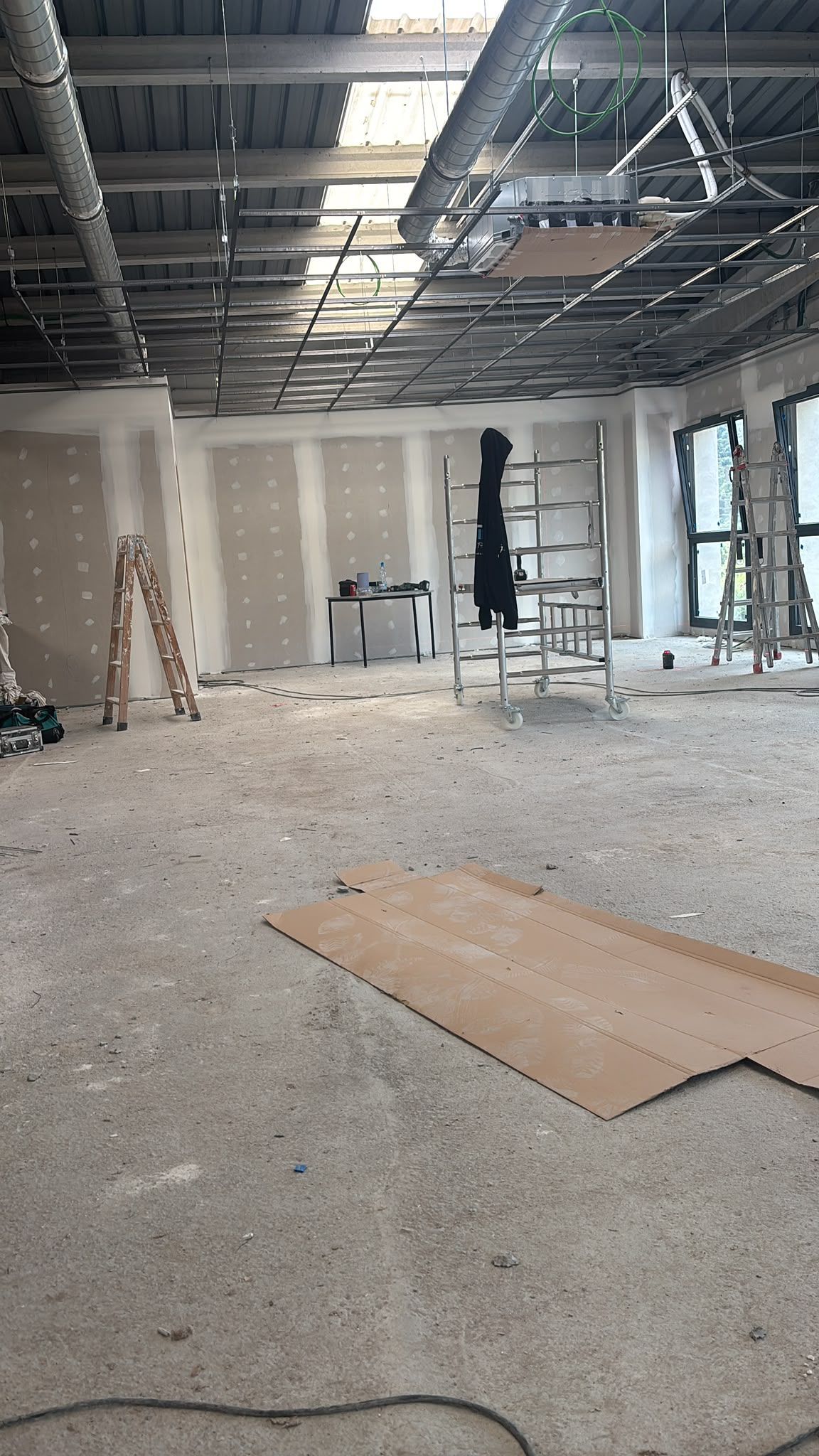 Interior de obra vacío con techo expuesto, escombros en el suelo y escaleras cerca de paredes sin terminar.