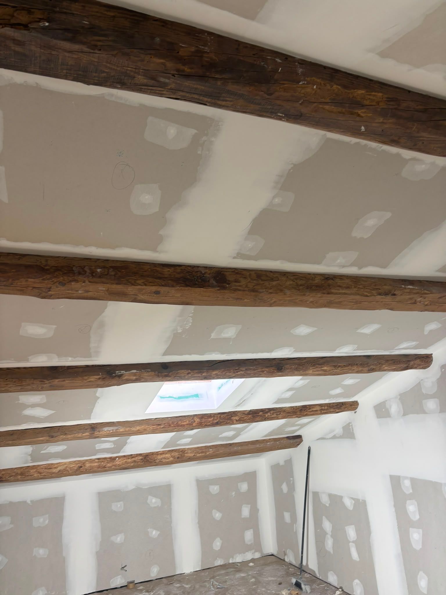 Ático sin terminar con paneles de yeso, vigas de madera a la vista y juntas selladas con cinta adhesiva en techos