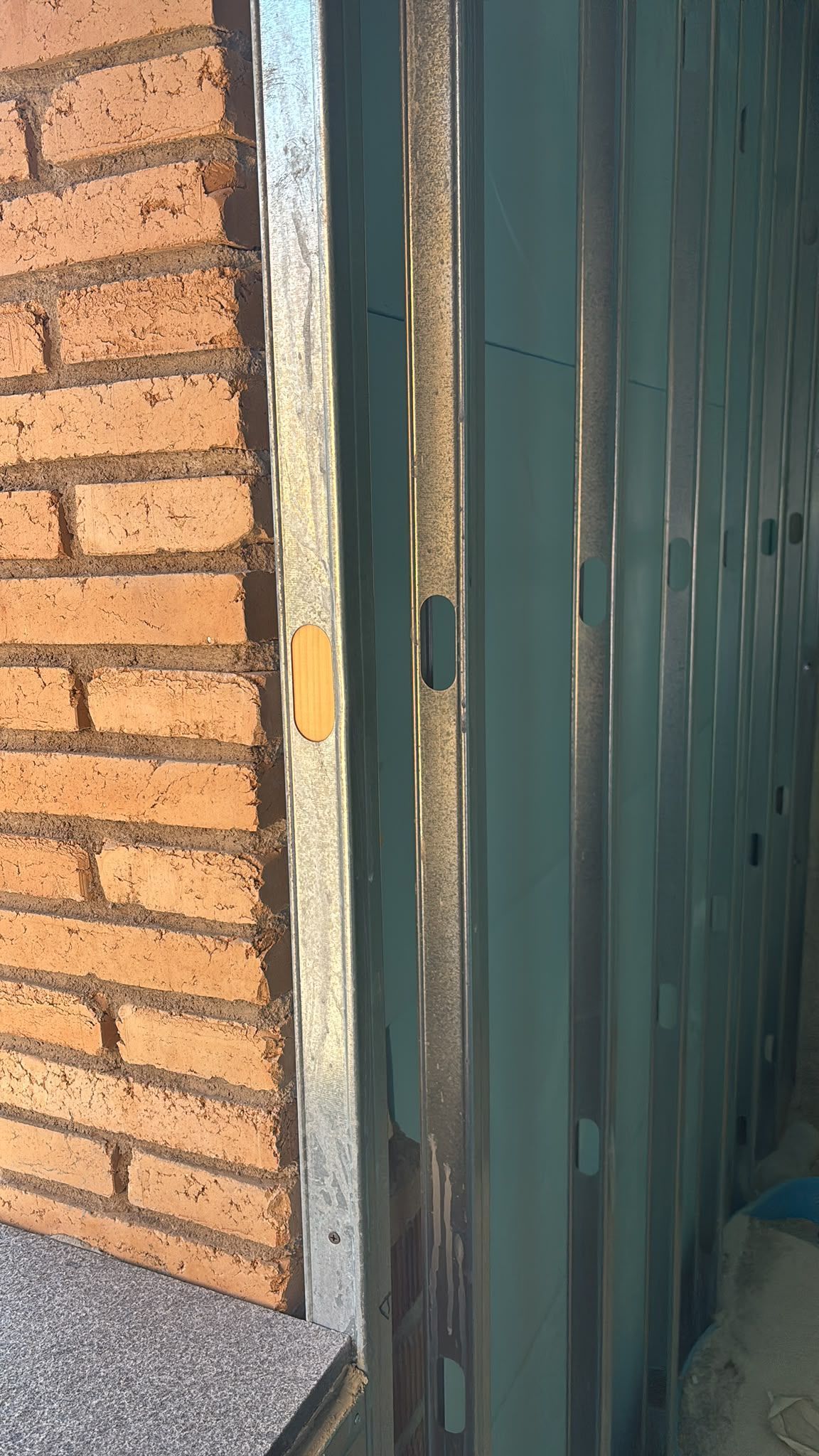 Primer plano de una pared de ladrillos junto a un marco de puerta de metal verde con la pintura desconchada 