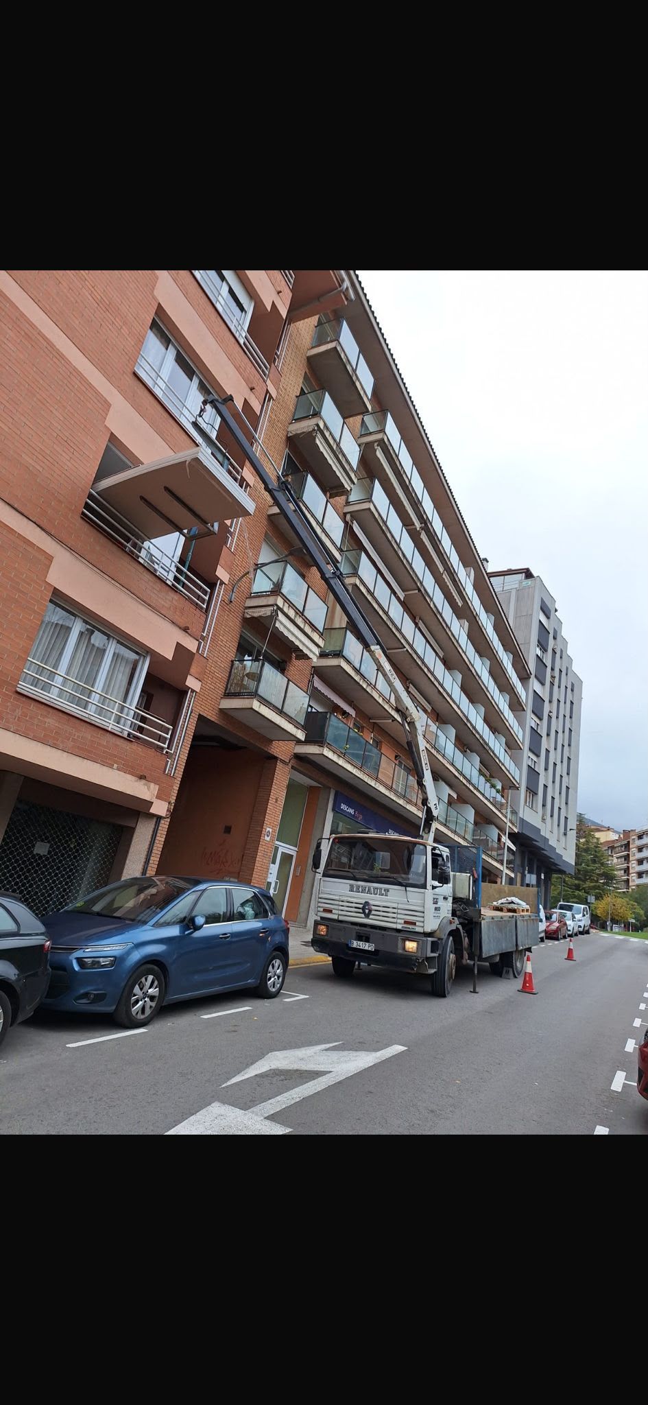 Vista de la calle de un edificio de apartamentos de ladrillo con coches aparcados a lo largo de una calle estrecha.