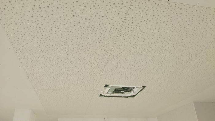 Un techo de color beige con una pequeña abertura empotrada y una rejilla de ventilación