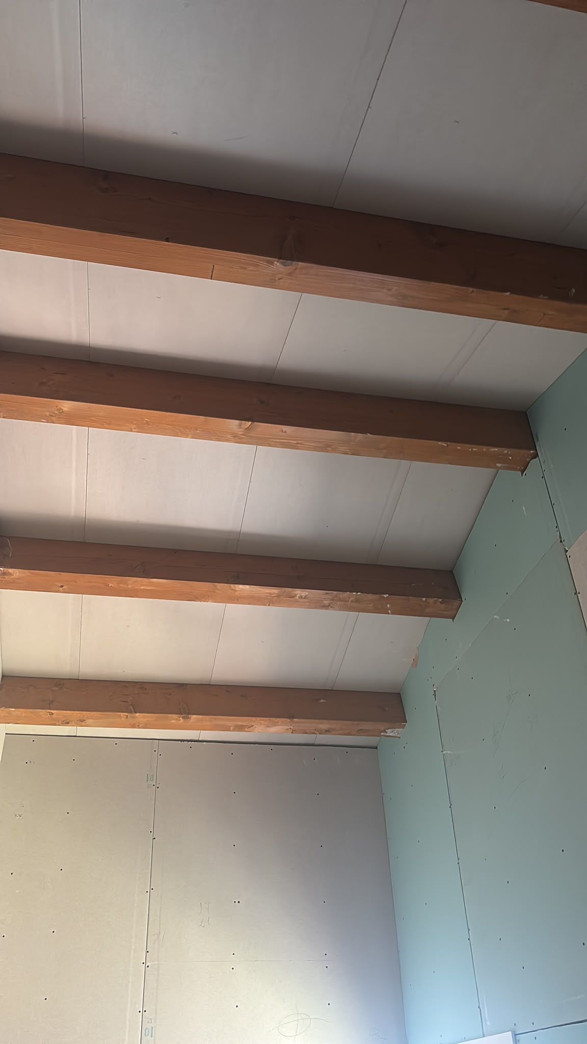 Esquina de pared blanca con vigas de madera a la vista en el techo y una pared lateral de color verde menta.