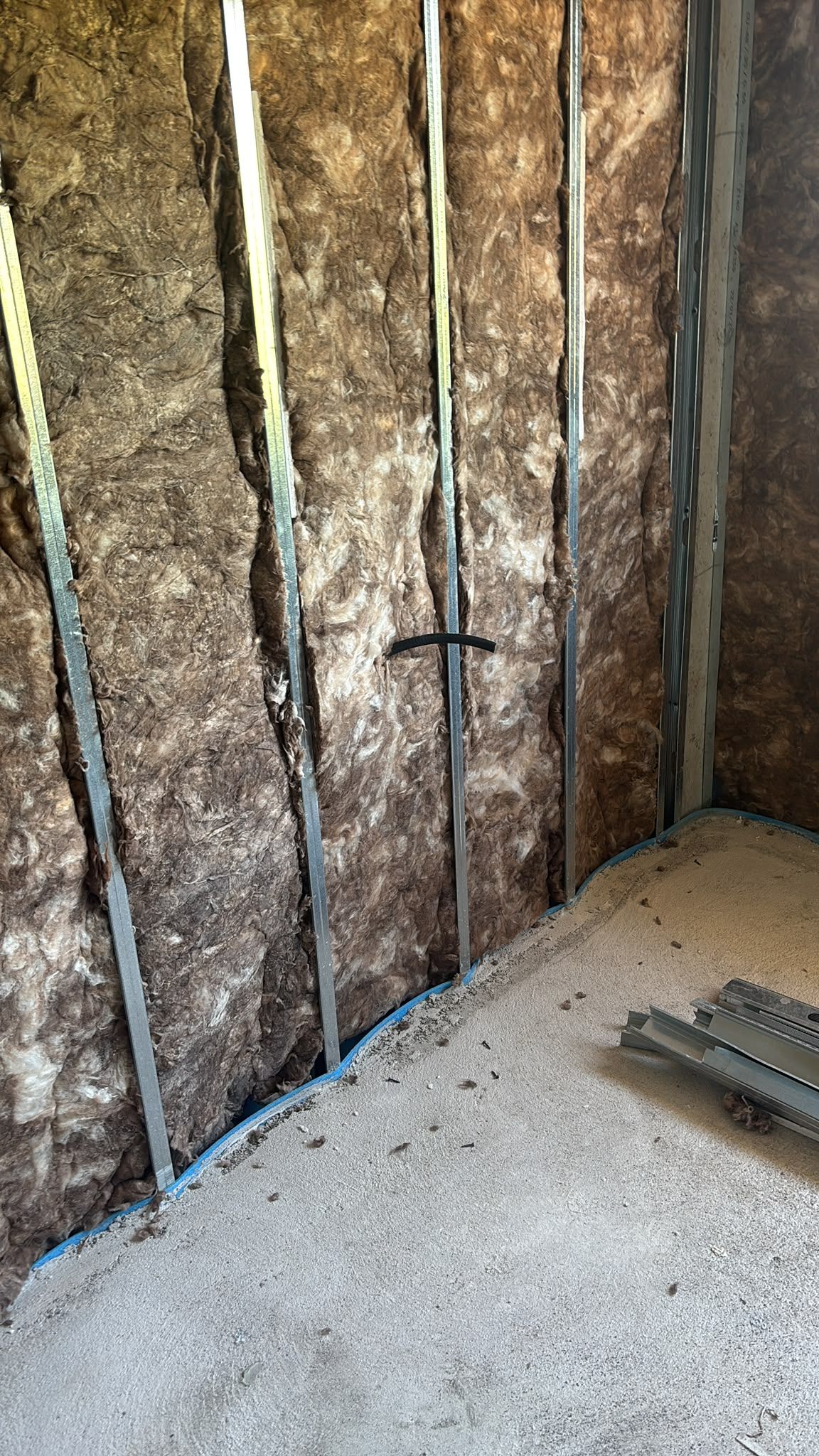 Estructura de pared aislada en un espacio de construcción, con montantes expuestos y piso de concreto rugoso.