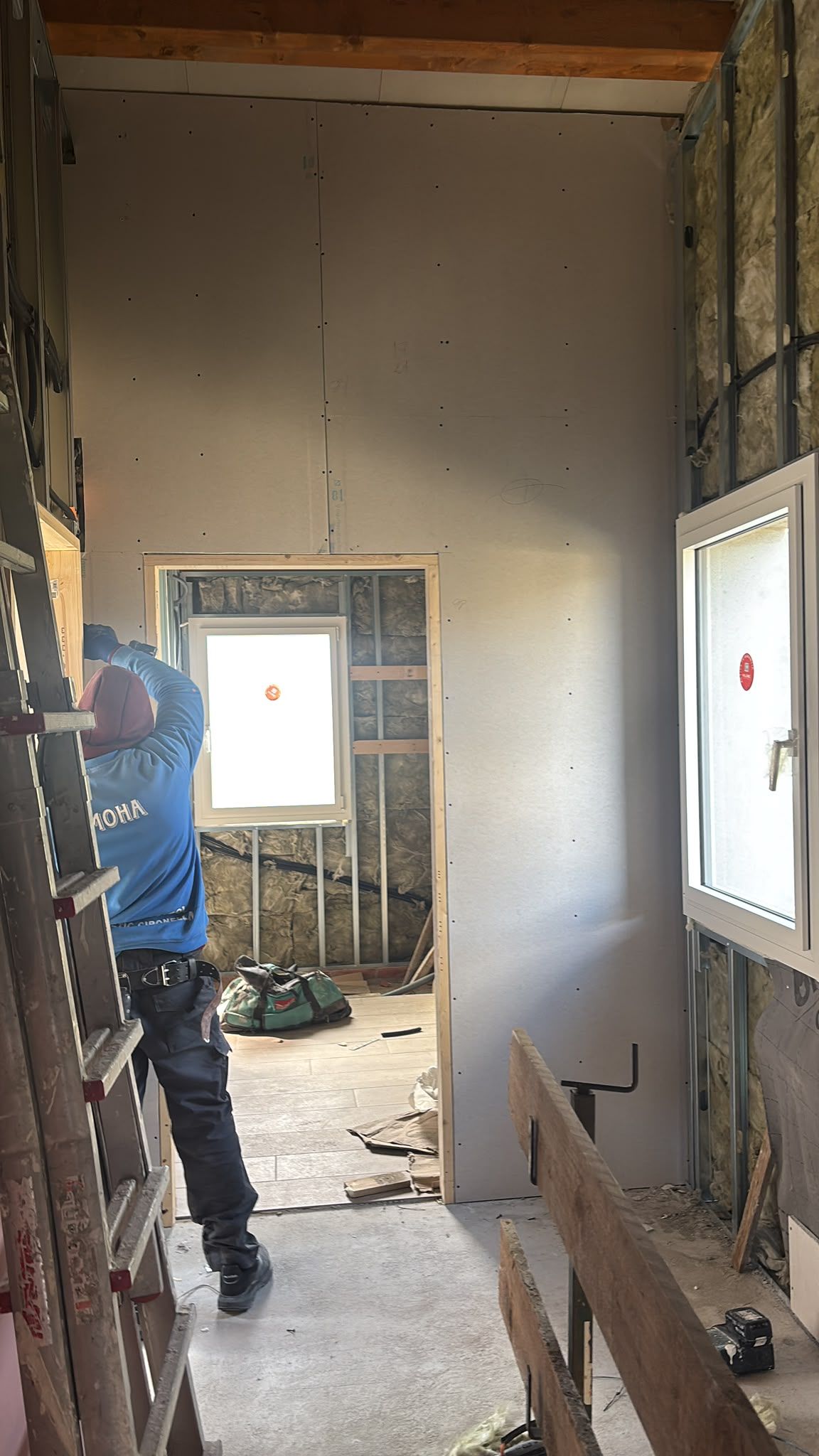 Pasillo parcialmente renovado con vigas a la vista, paneles de yeso, un trabajador y ventanas luminosas a ambos lados.