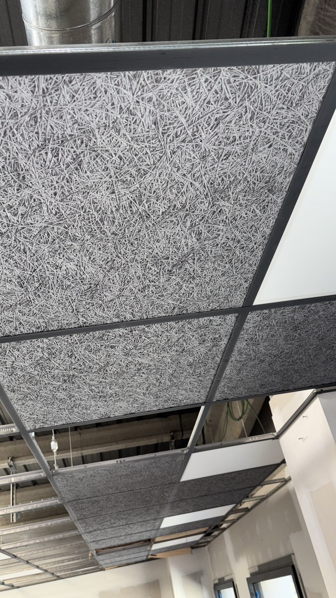Paneles acústicos para techo y conductos de ventilación a la vista en la vista del techo de un pasillo o una oficina.