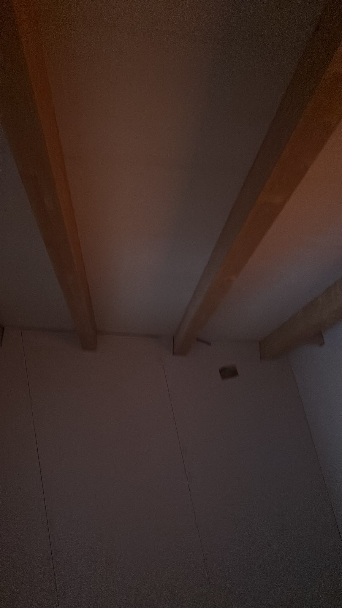 Techo de habitación con poca luz, vigas de madera a la vista y una pequeña lámpara de pared