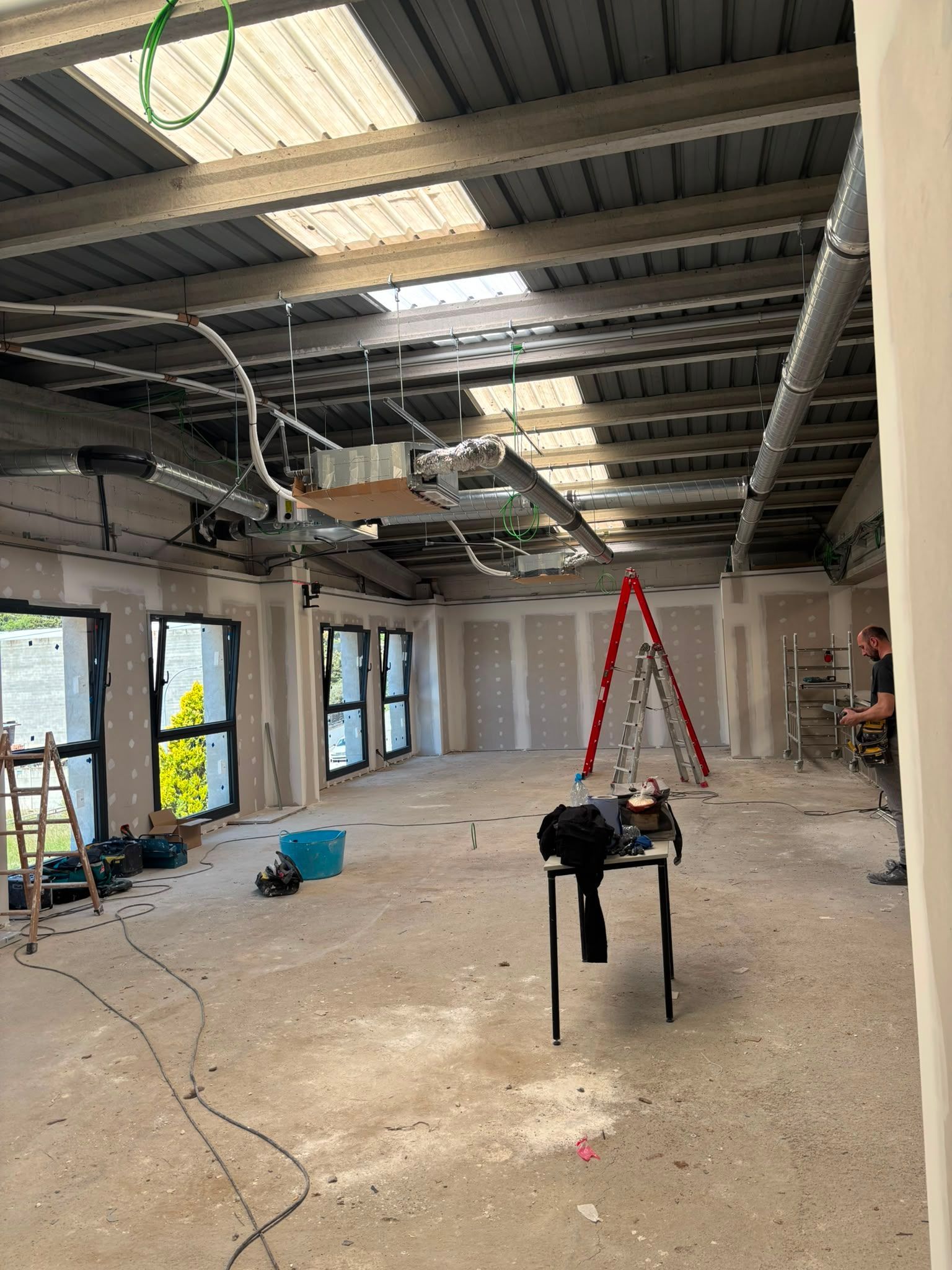 Interior industrial reformado con techo a la vista, ventanas, escalera y herramientas de construcción en el suelo.