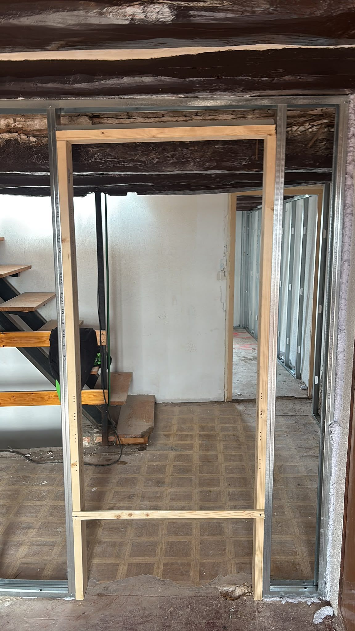Entrada sin terminar que enmarca una habitación en renovación, con vigas a la vista y suelo de hormigón.