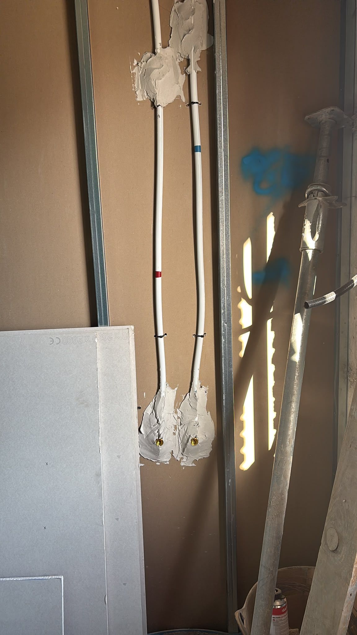 Cableado y conductos expuestos en una habitación sin terminar con un panel de yeso inclinado hacia la izquierda.