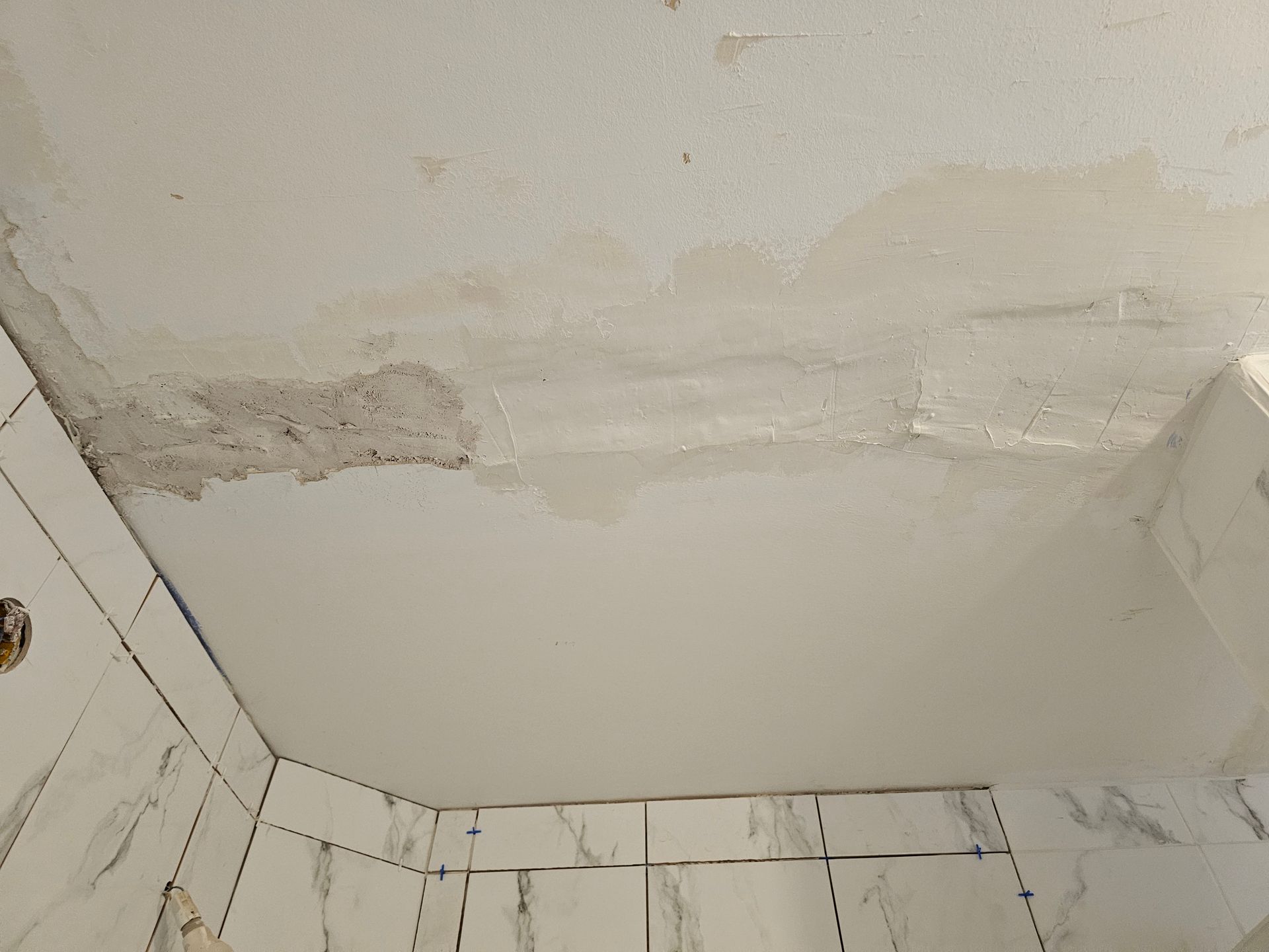Plafond qui se décolle et dégâts d'eau au-dessus des murs carrelés blancs de la salle de bains
