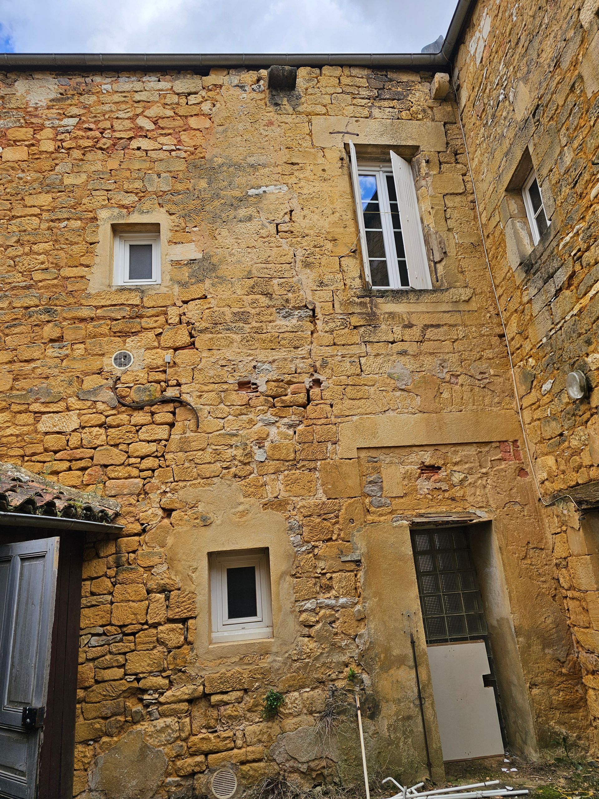 Vieux mur d'une maison en pierre jaune avec de petites fenêtres et une porte ouverte sous un ciel nuageux