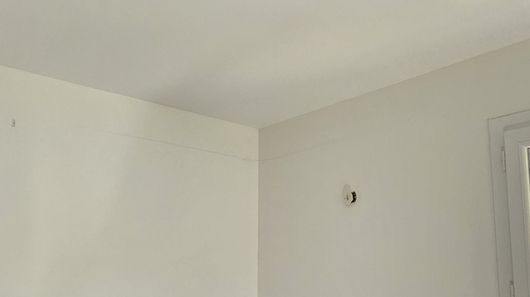 Coin de pièce blanc nu avec un petit crochet mural et une partie du cadre de la fenêtre visibles