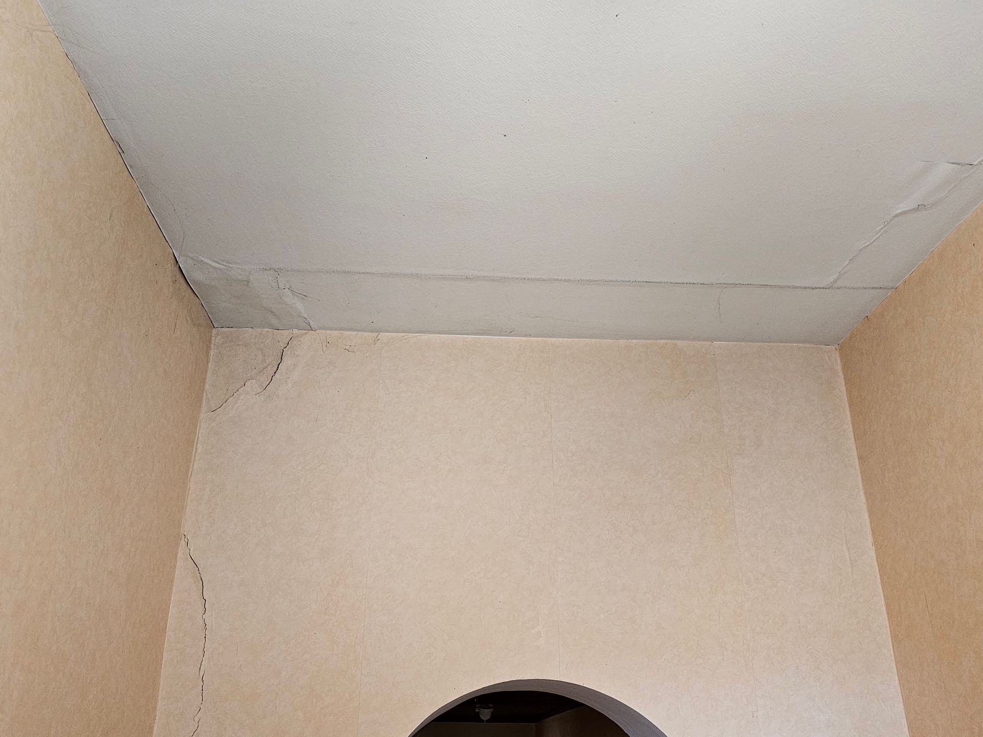 Coin d'une pièce beige avec un plafond gris en mauvais état et une petite ouverture cintrée au centre, en bas.