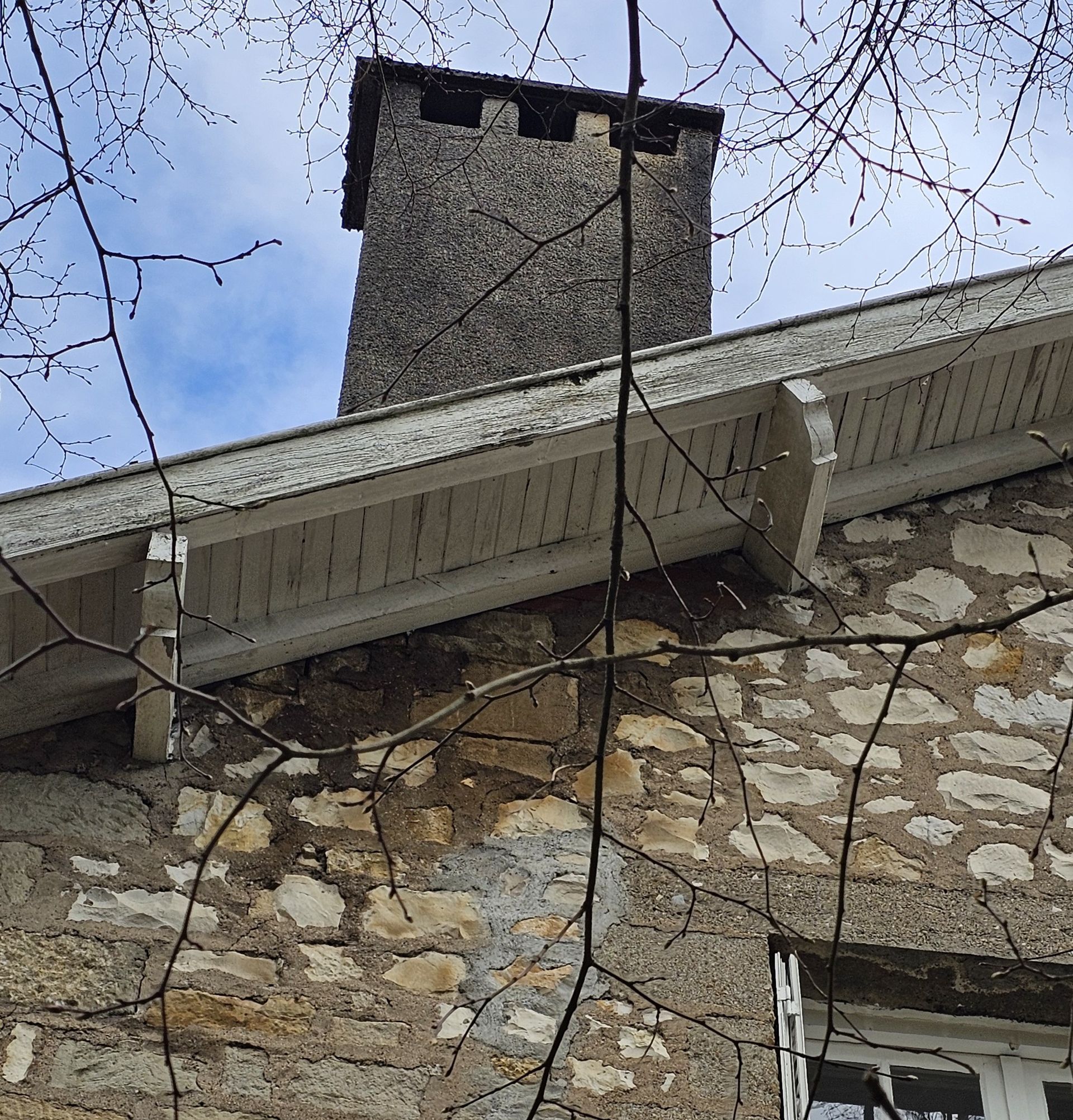 Toiture d'une maison avec une haute cheminée en briques se détachant sous un ciel nuageux.