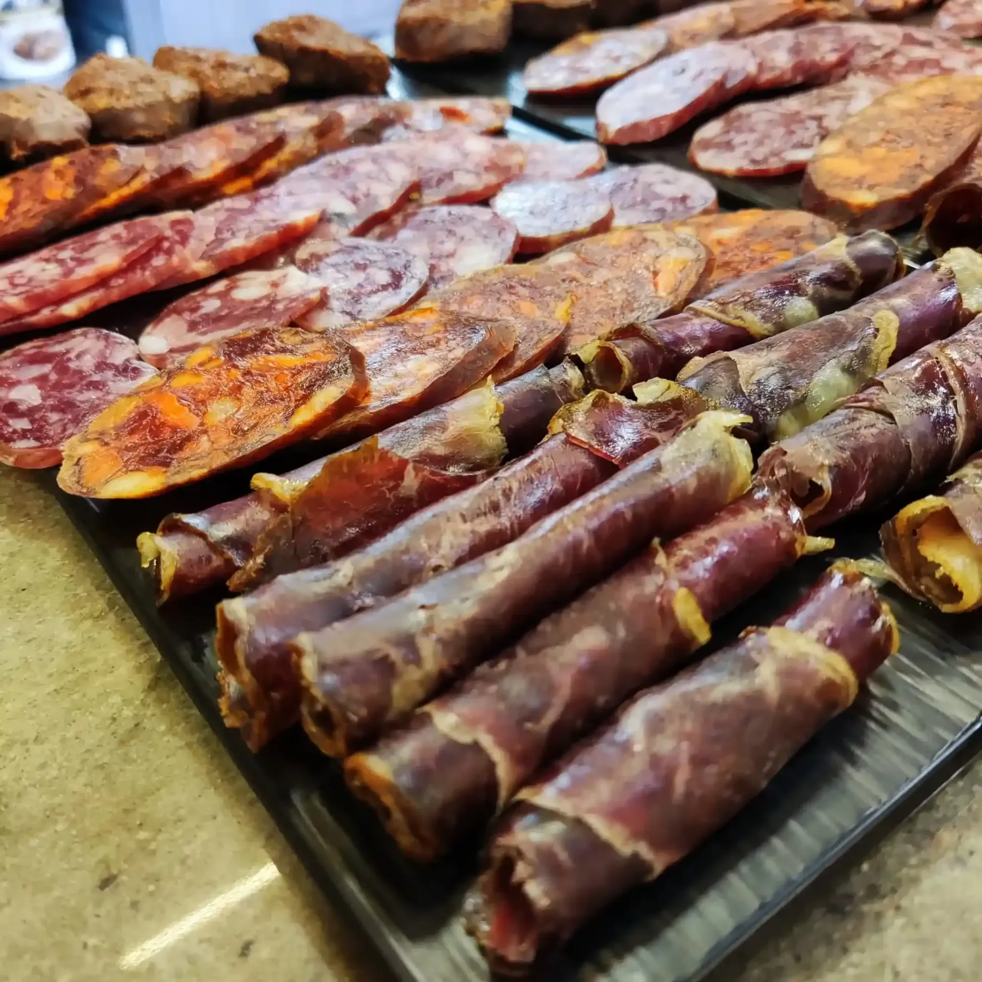 Bandeja con lonchas de carne seca variadas y tiras de carne enrolladas sobre un mostrador.