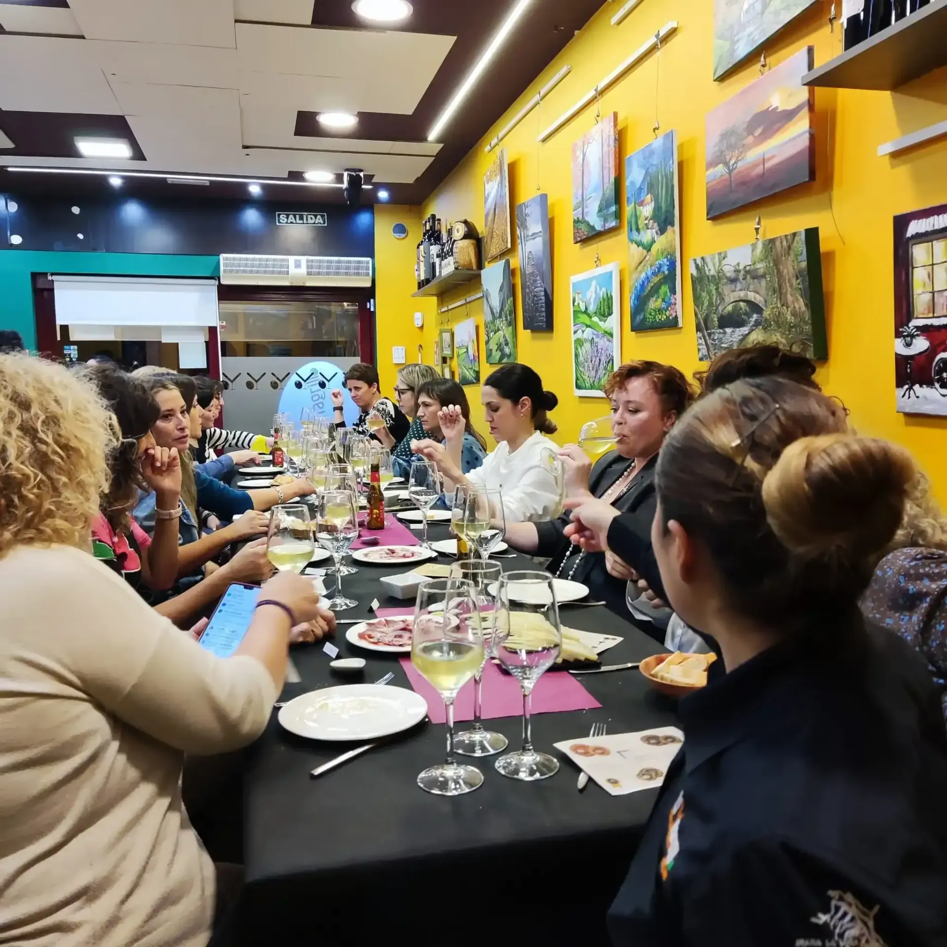 Varias personas sentadas en una larga mesa de comedor en un restaurante colorido, compartiendo una comida y una conversación.
