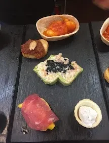 Surtido de sushi colorido y pequeños aperitivos dispuestos en una bandeja oscura.
