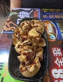 Primer plano de comida a la parrilla con salsa en una bandeja negra sobre una mesa cubierta con coloridas revistas.