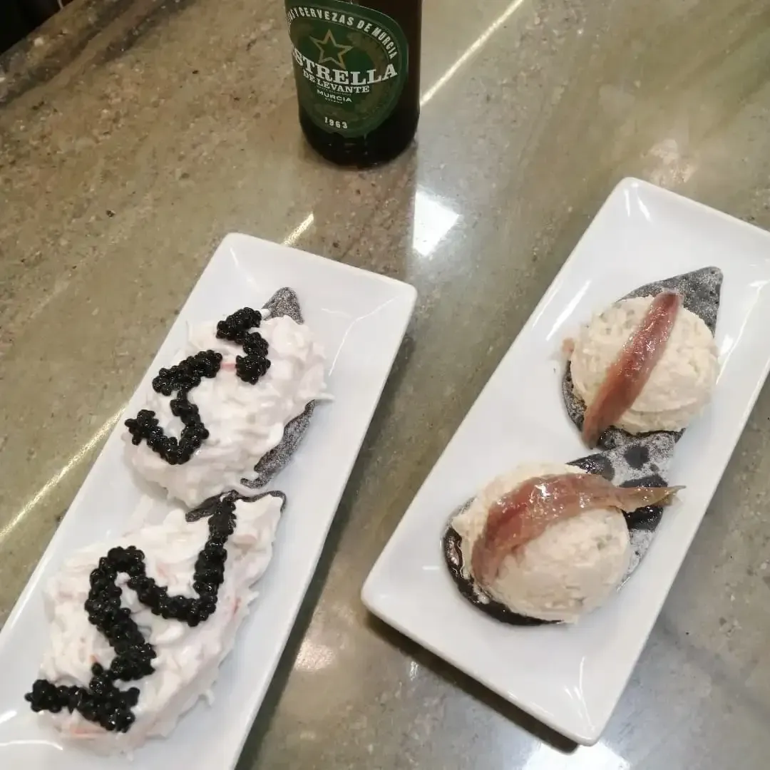 Postres en platos blancos con sirope de chocolate y frutos rojos sobre una encimera, con una botella de cerveza cerca.
