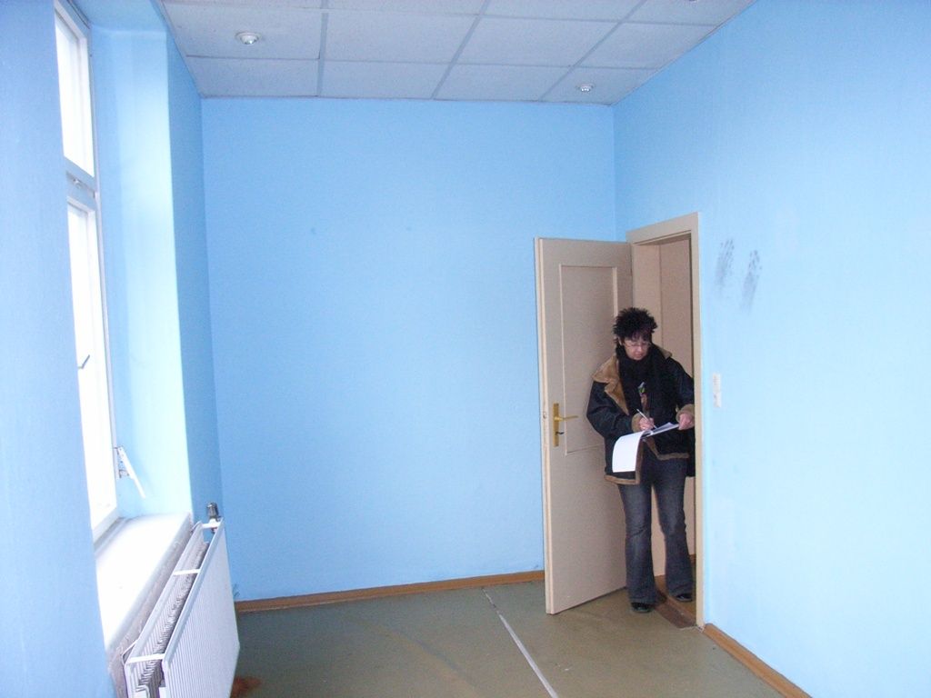 Frau Wedermann (Geschäftsführerin) steht in einem Raum mit blauen Wänden und macht sich Notizen.