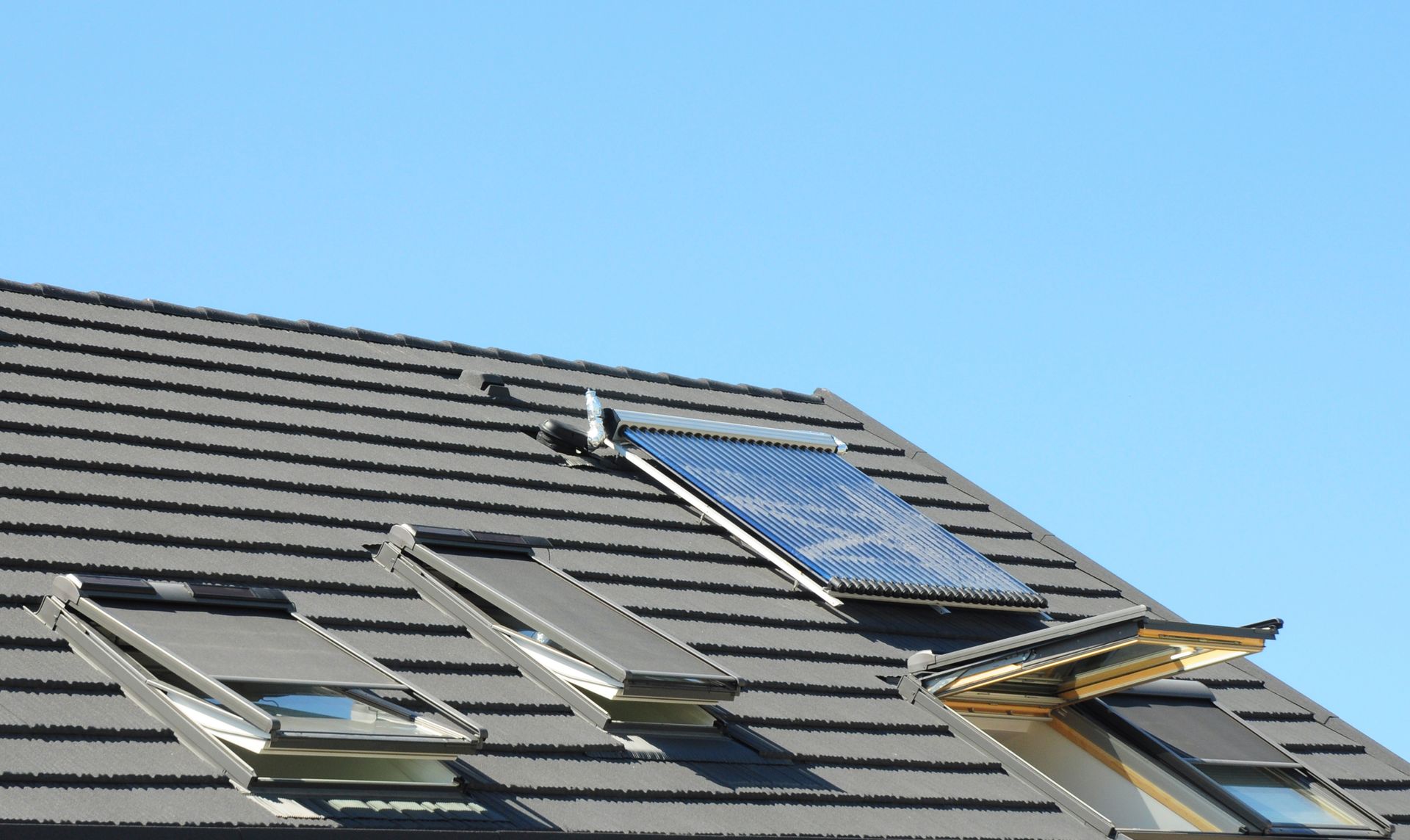 Un toit en tuiles avec trois fenêtres de toit et un panneau solaire.