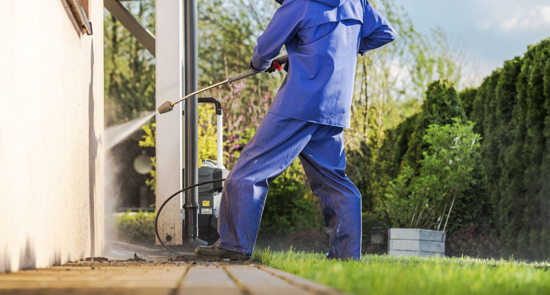 Une personne vêtue d'une combinaison de protection bleue utilise un nettoyeur à haute pression pour une façade.