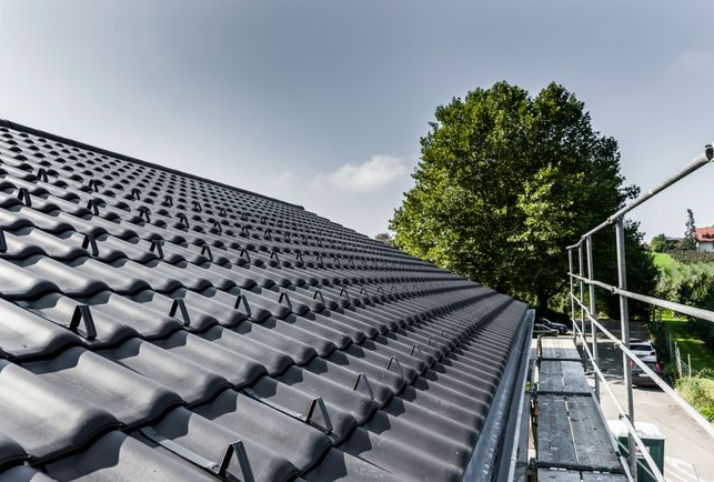 Gros plan sur un toit de tuiles gris foncé avec des échafaudages visibles sur la droite.