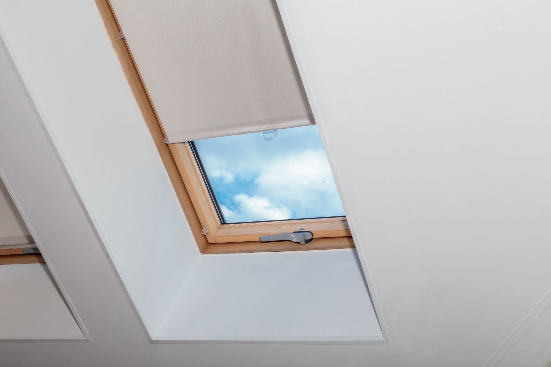 Une fenêtre de toit encastrée dans un plafond blanc, avec un cadre en bois et un store beige.