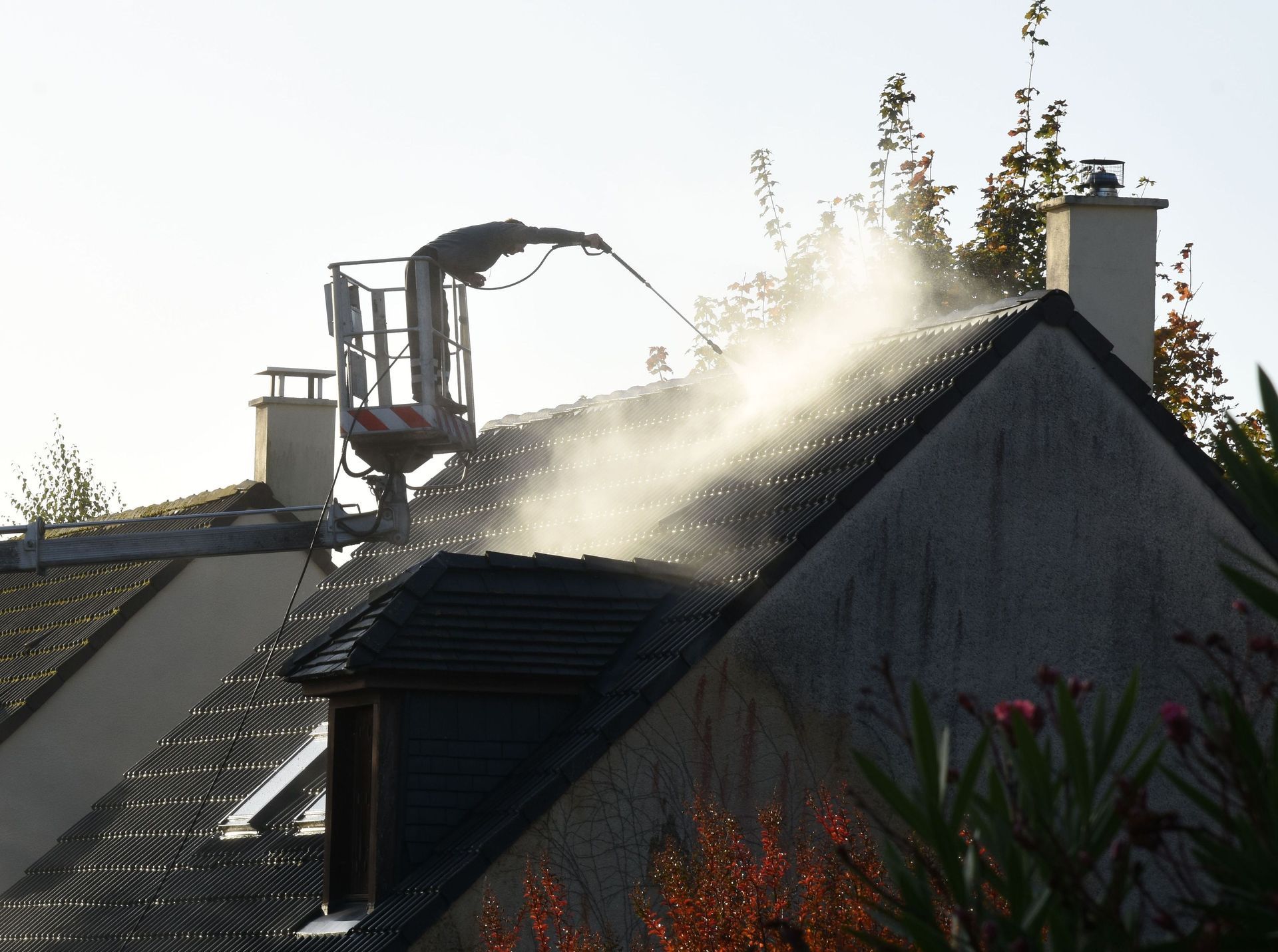 Un ouvrier, dans une nacelle élévatrice, utilise un nettoyeur haute pression pour nettoyer un toit.