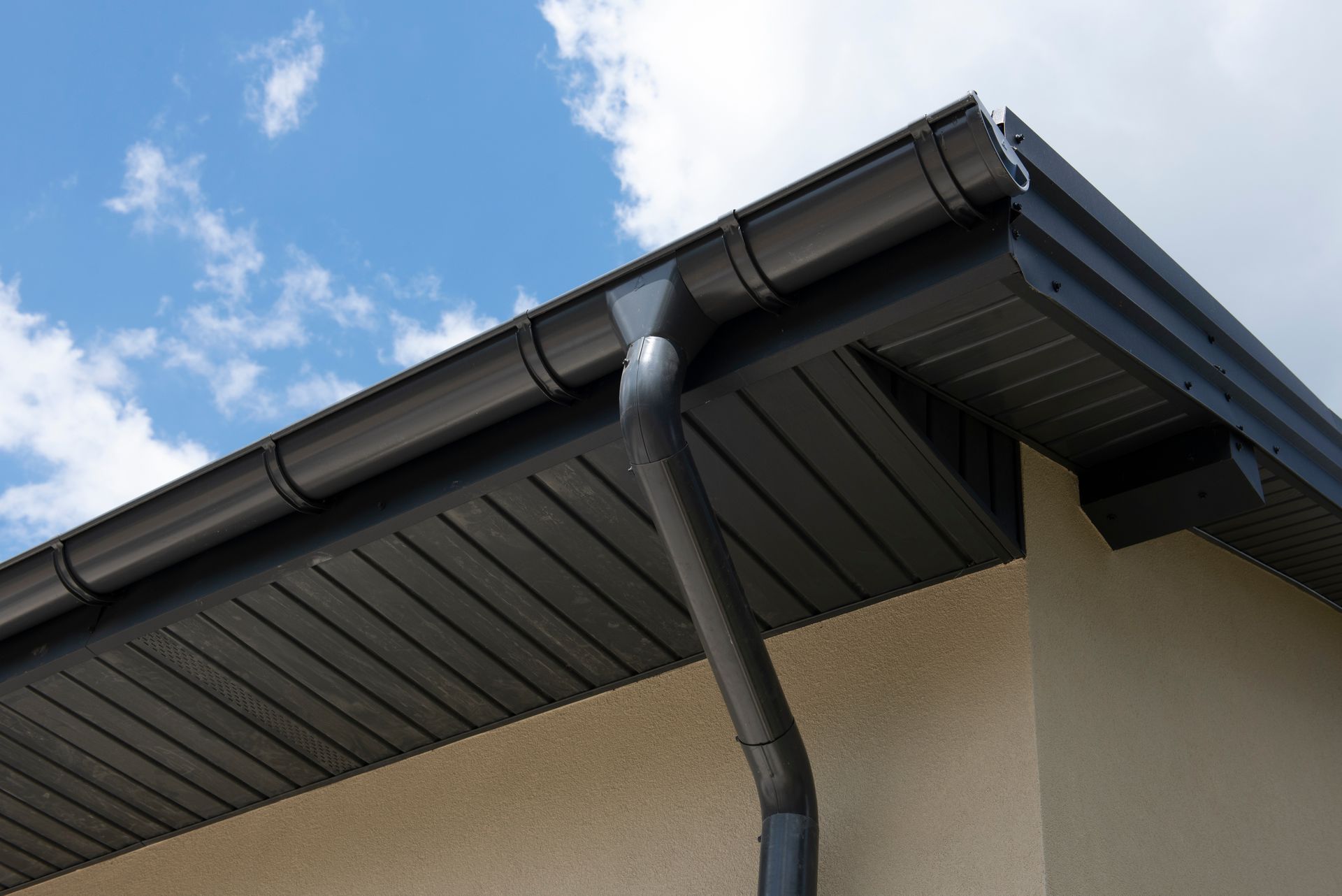 Une gouttière et un tuyau de descente gris foncé fixés au mur extérieur d'une maison.