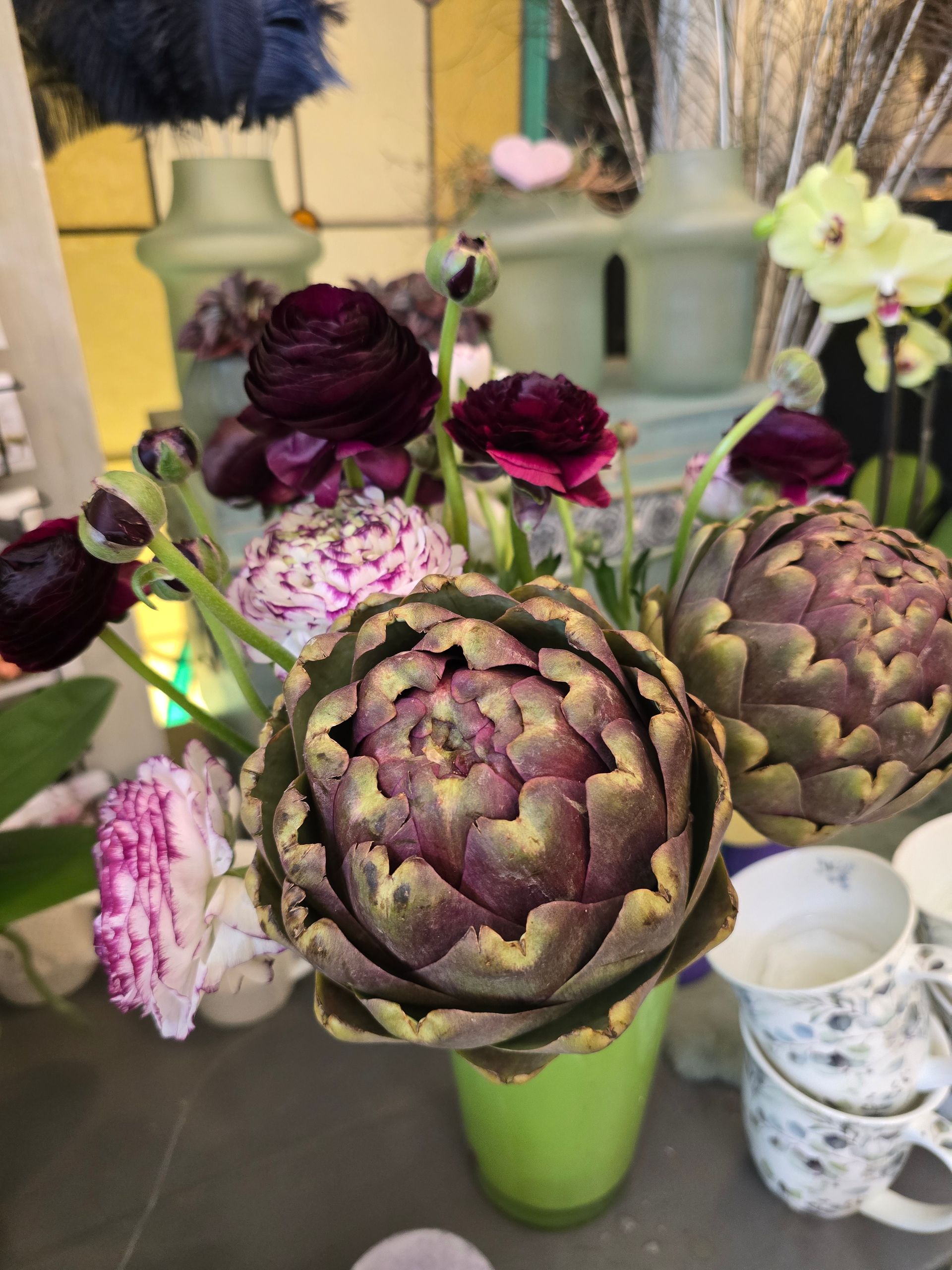 Artischocken und Blumen in einer grünen Vase auf einem Tisch