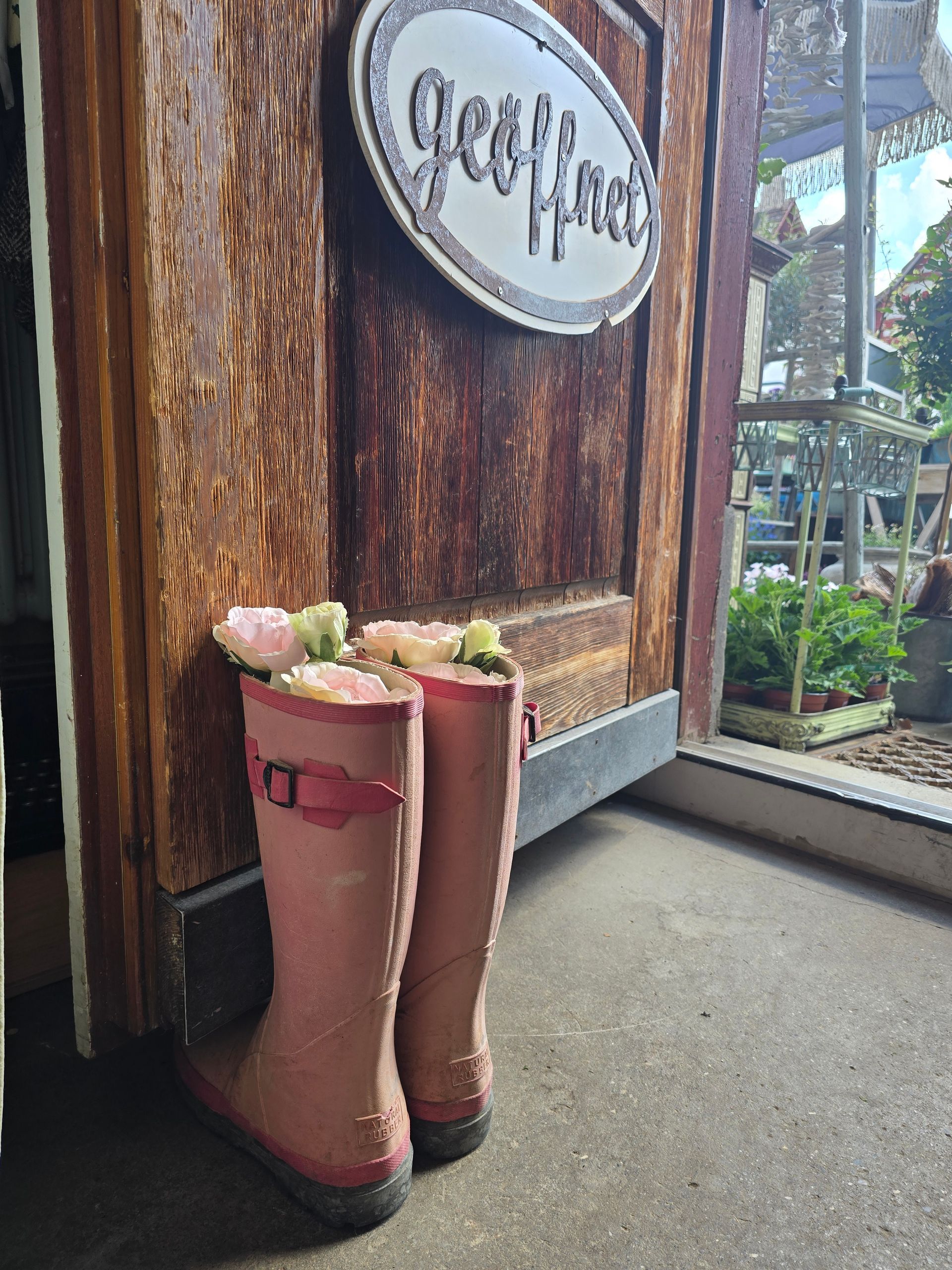Ein Paar rosa Gummistiefel mit Blumen darin lehnt an einer Holztür.