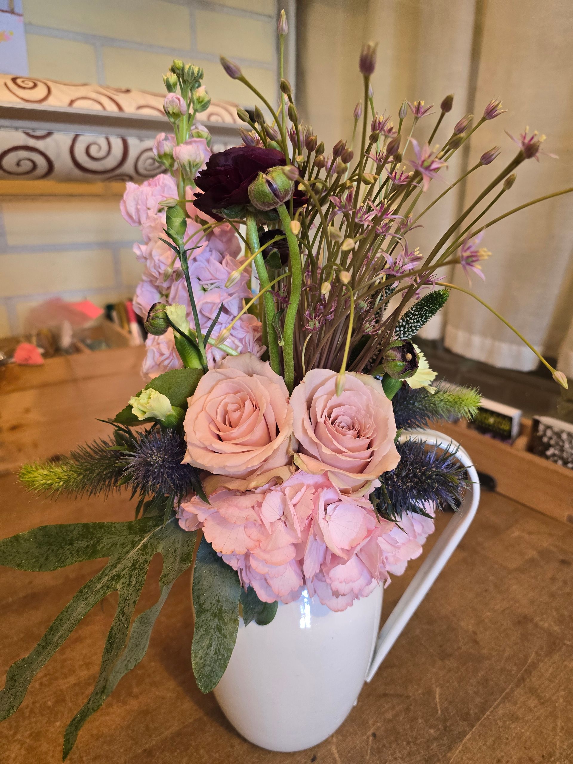 Auf einem Holztisch steht ein mit rosa Blumen gefüllter Krug.