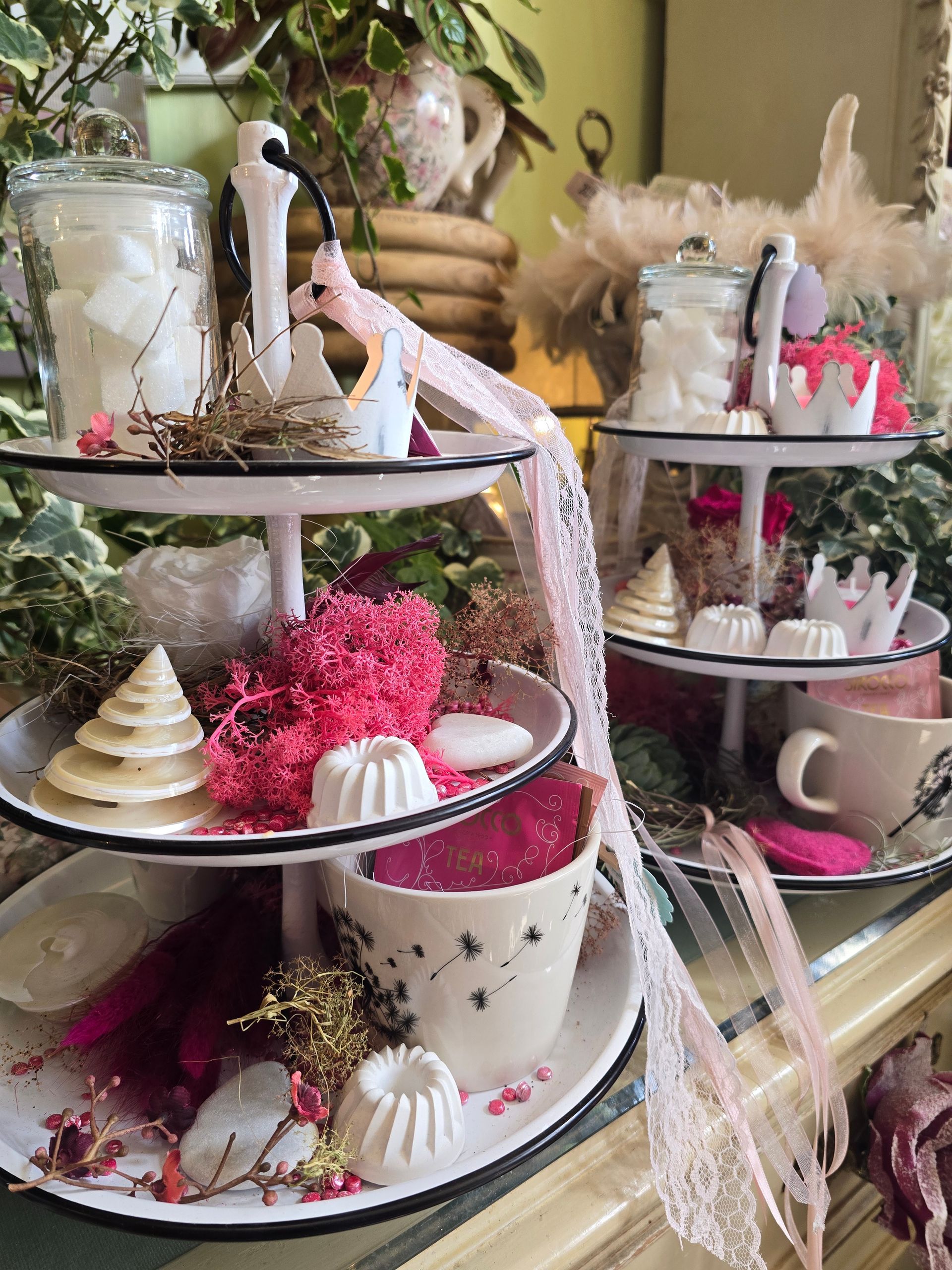 Ein dreistöckiges Tablett gefüllt mit Kerzen, Tassen und Blumen.