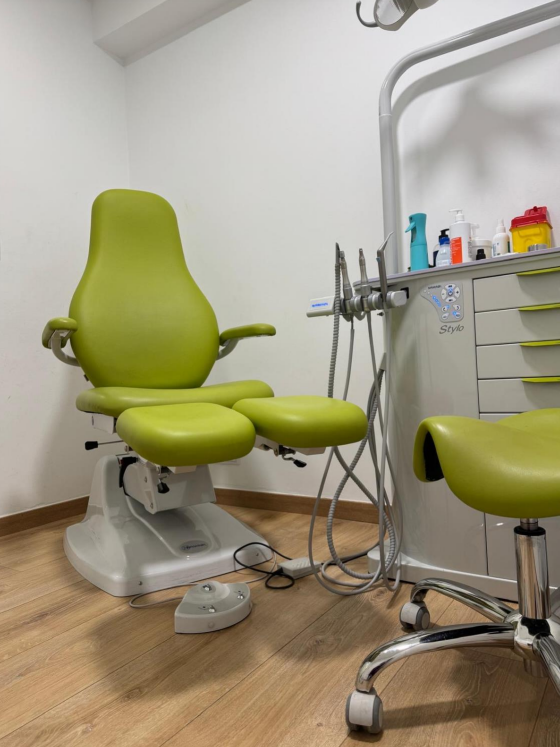 Una silla verde en un consultorio dental con un taburete al lado.