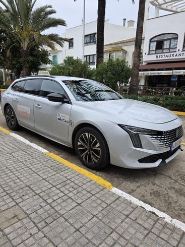 Un sedán blanco estacionado junto a la acera en una calle de la ciudad con edificios y palmeras cerca.