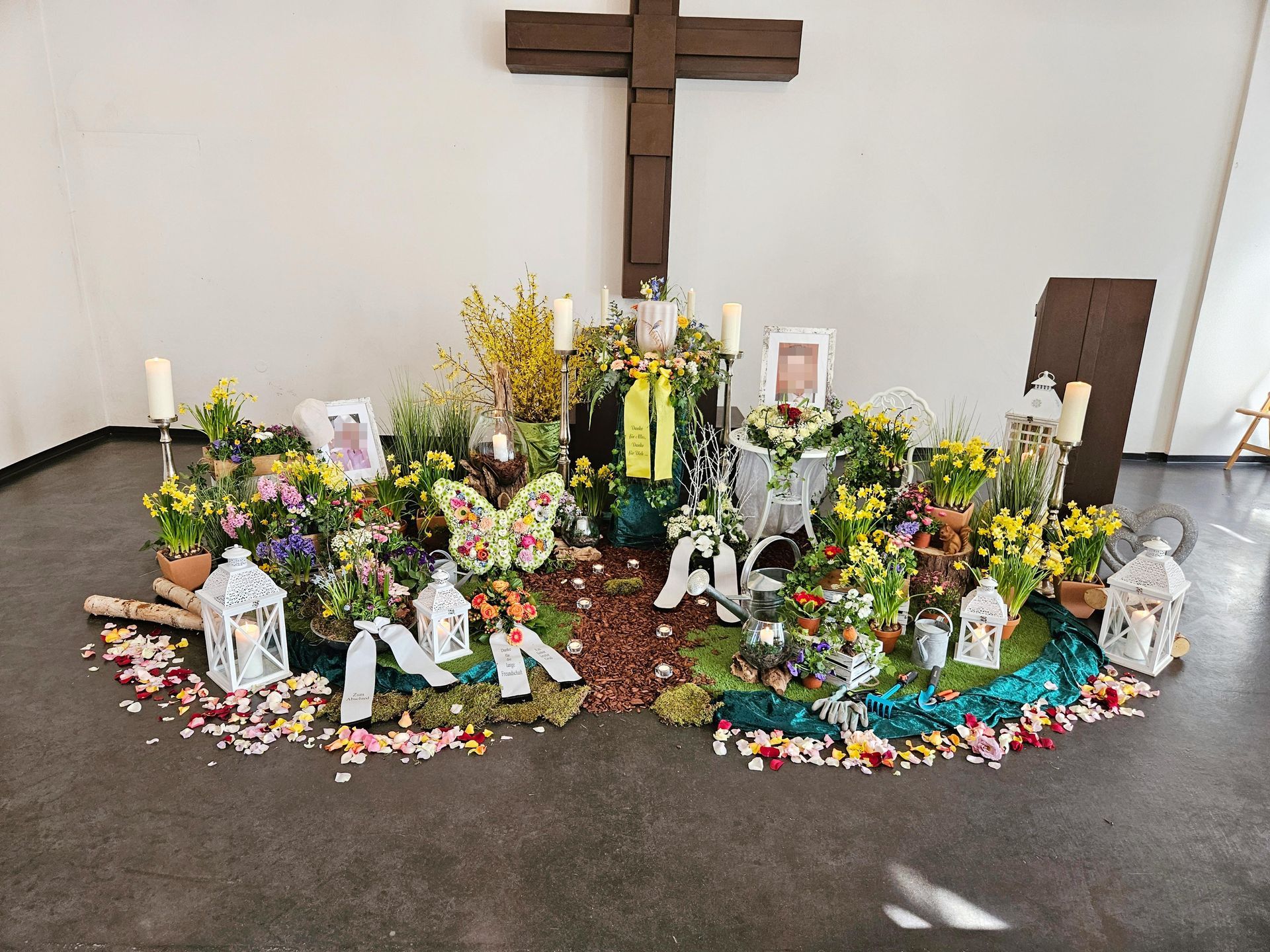 In einem Raum ist ein Kreuz von Blumen und Kerzen umgeben.