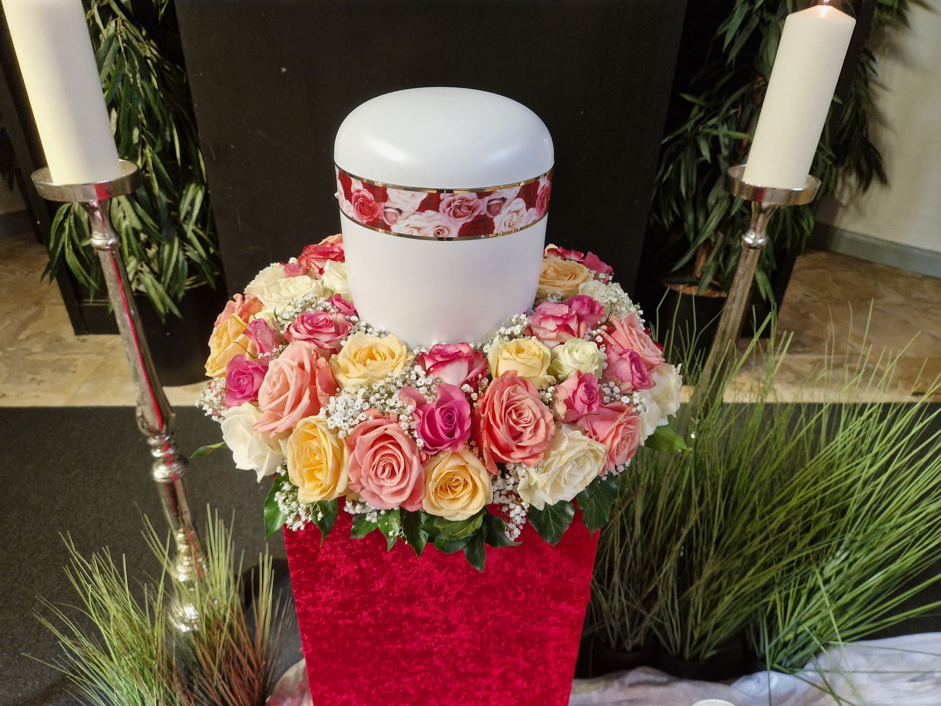 Eine weiße Urne ist von Blumen und Kerzen umgeben.