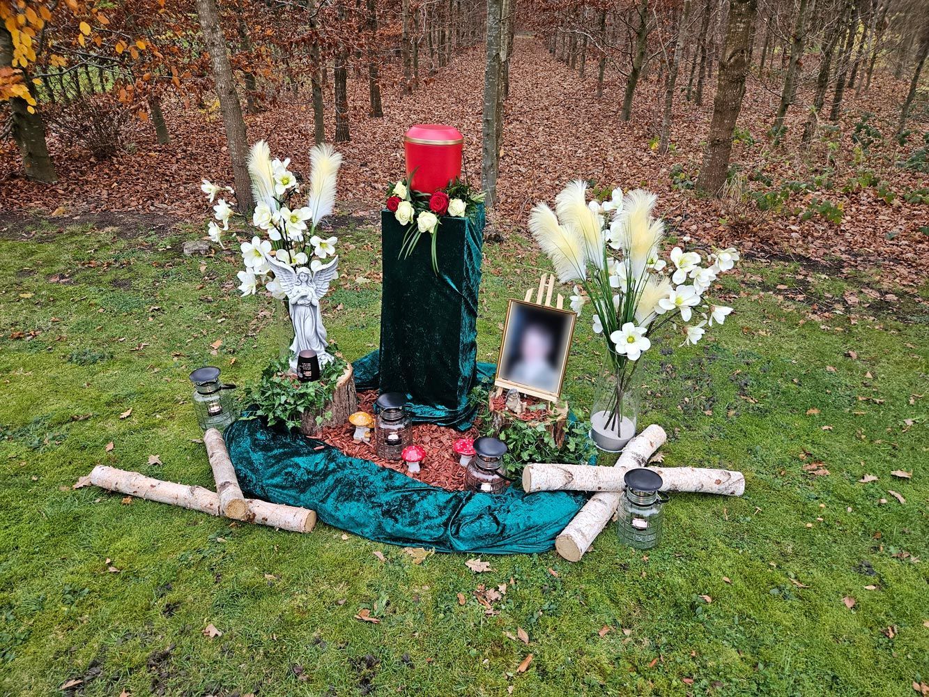 Ein Denkmal mit Kerzen, Blumen, einem Bild und einem Kreuz im Gras.