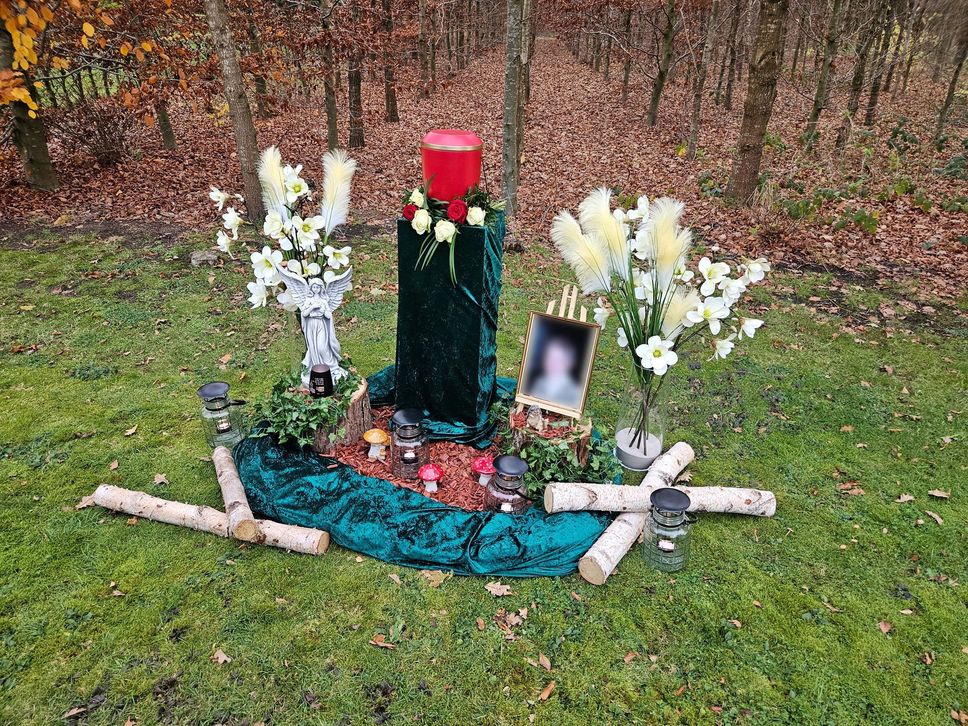 Ein Denkmal mit Kerzen, Blumen, einem Bild und einem Kreuz im Gras.