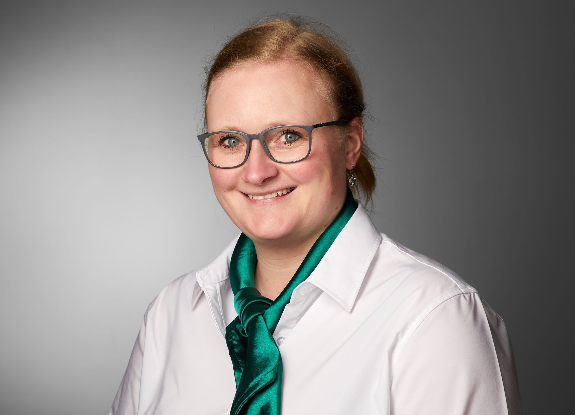 Eine Frau mit Brille und grünem Schal lächelt in die Kamera.