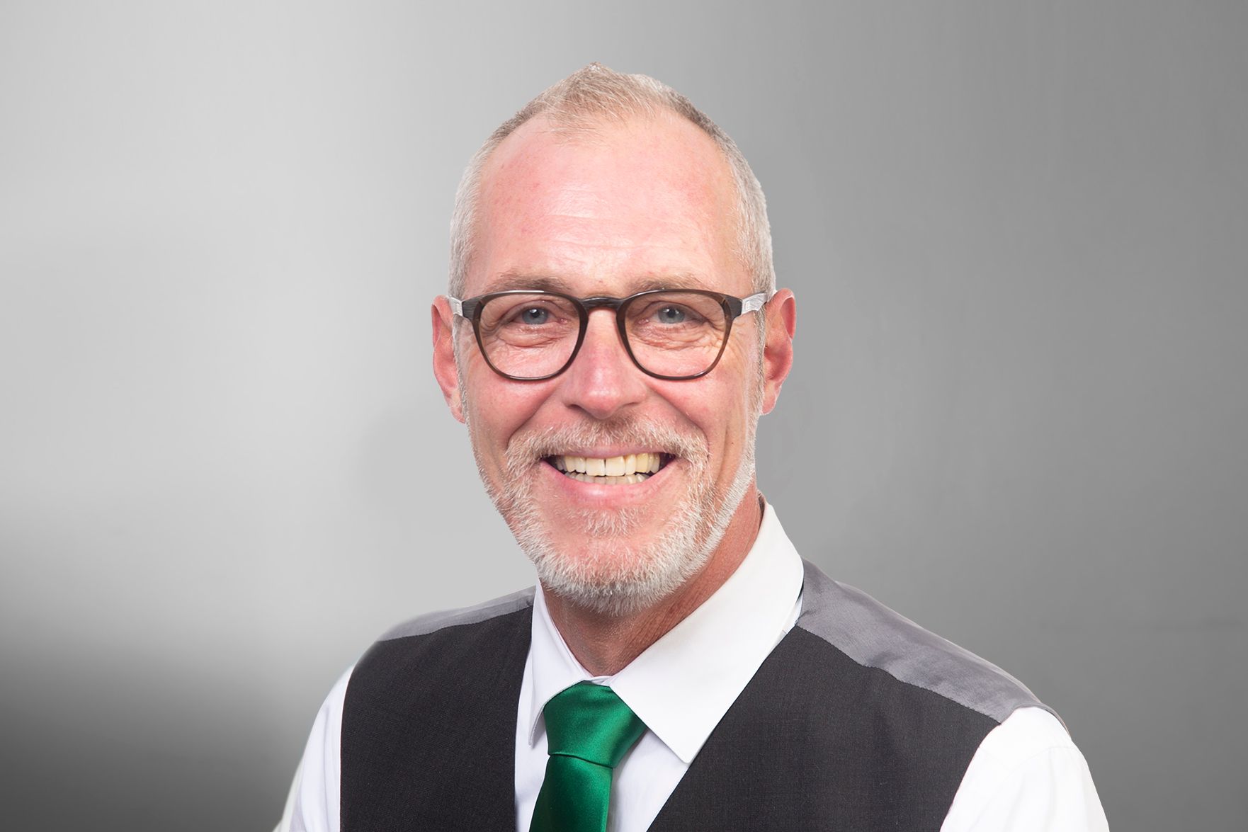 Ein Mann mit Brille und grüner Krawatte lächelt in die Kamera.