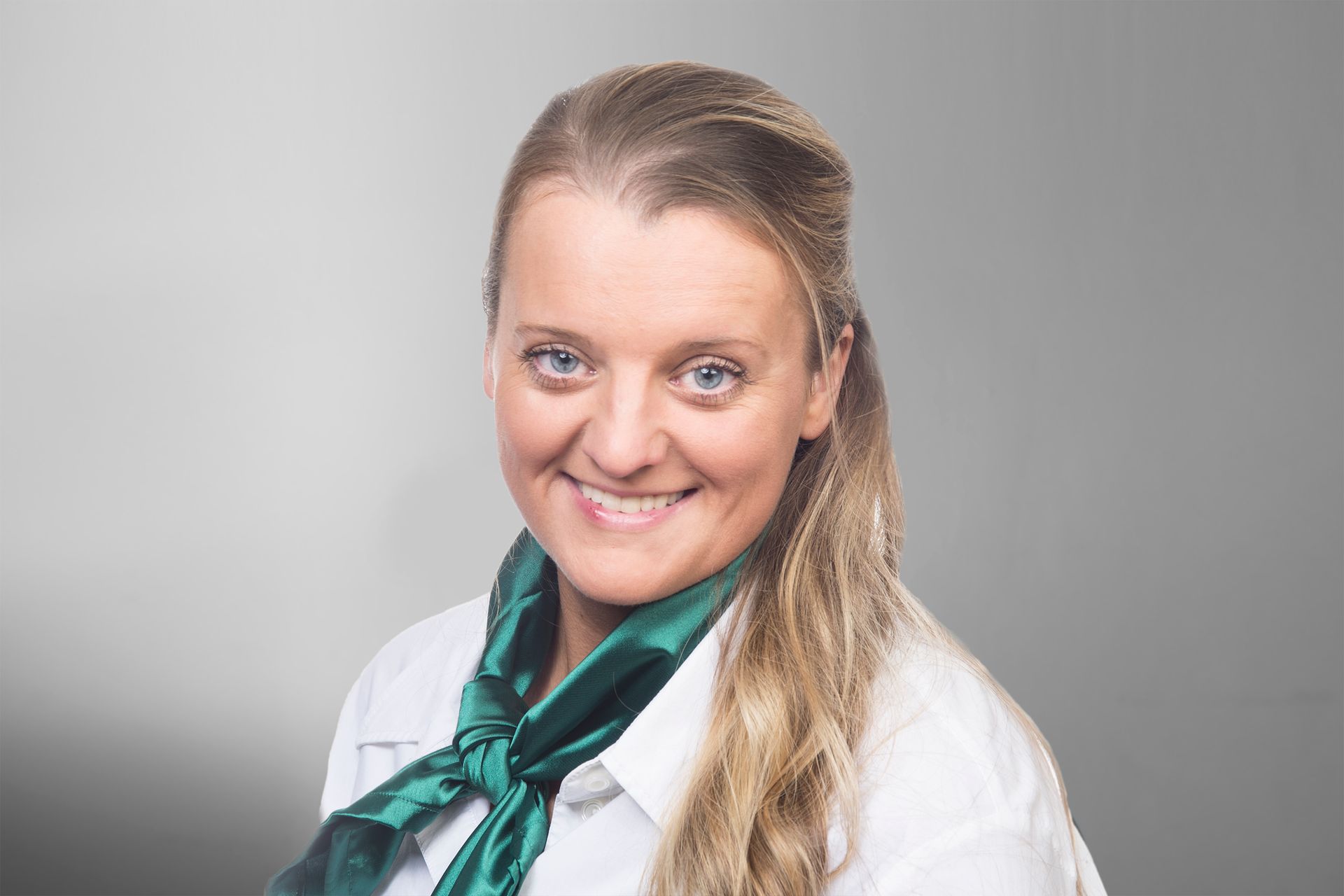 Eine Frau mit einem weißen Hemd und einem grünen Schal lächelt.